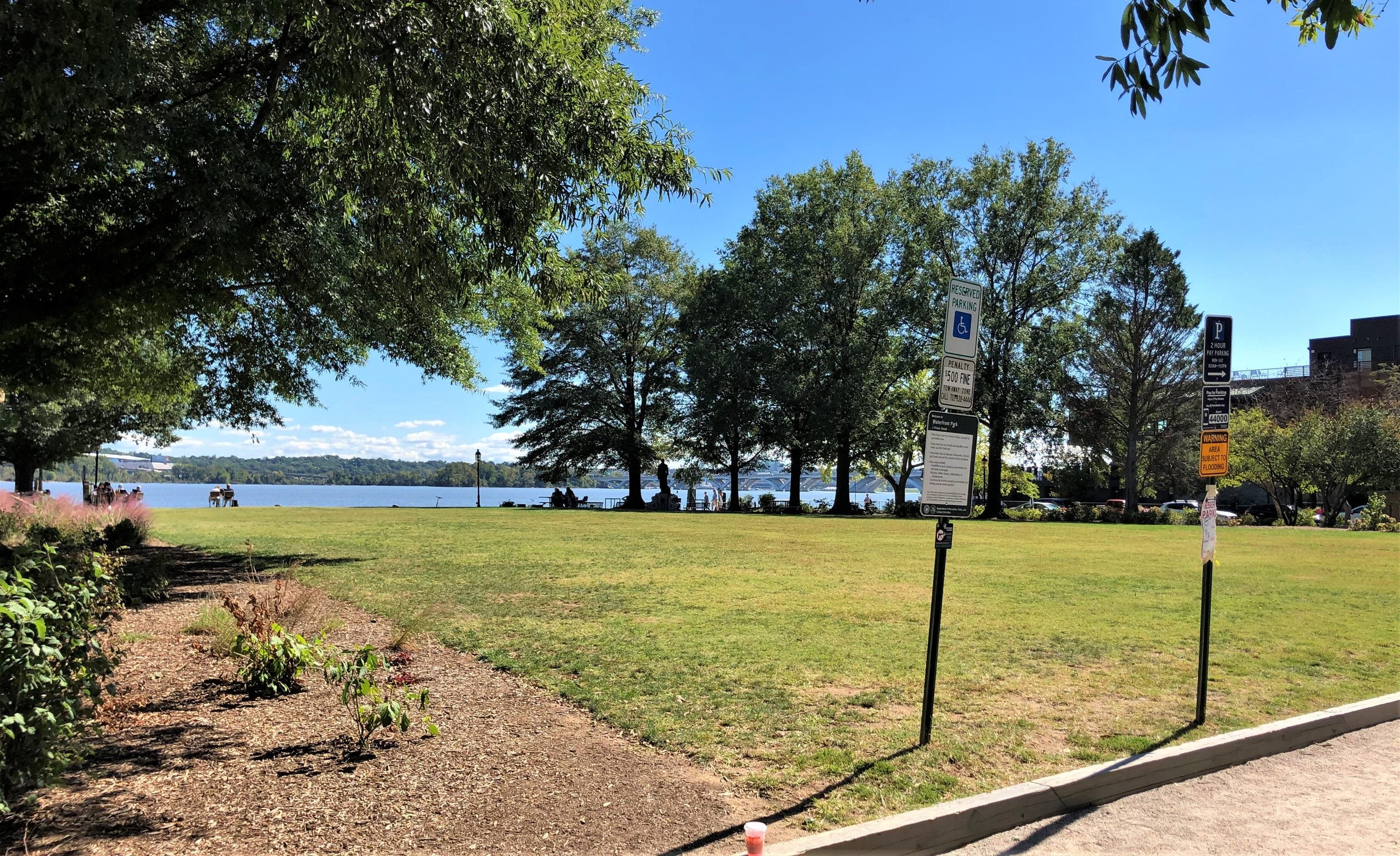A grassy park overlooking a river, with parking signs in the foreground.