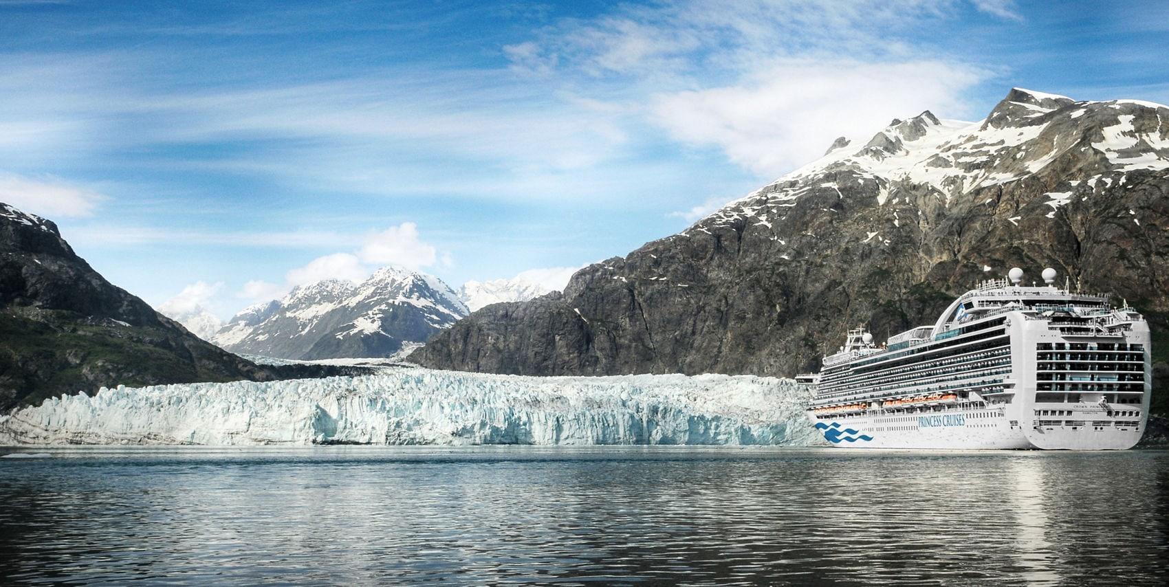 A large Princess Cruises ship sailing through water in front of a massive glacier with snow-capped mountains in the background.