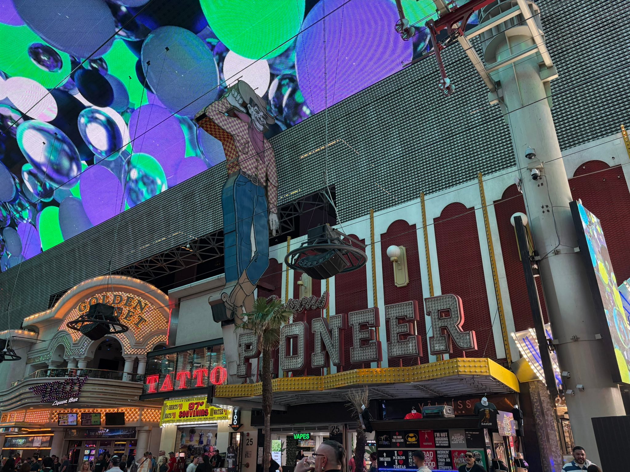 The Pioneer Saloon sign and the giant Vegas Vickie neon cowboy figure in front of a large, abstract LED canopy on the Fremont Street Experience.