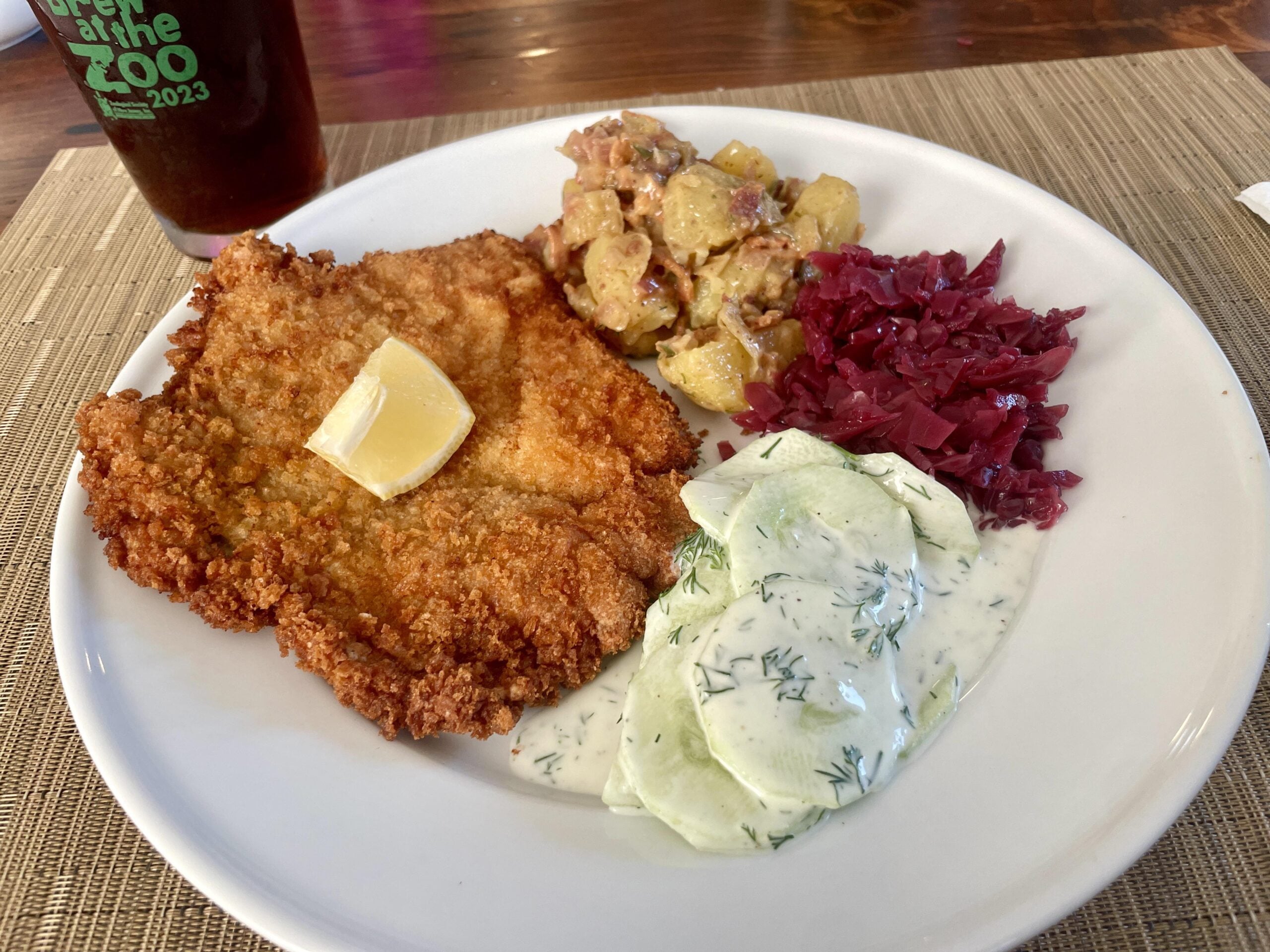 A plate featuring a breaded schnitzel with a lemon wedge, potato salad, red cabbage, and cucumber salad with dill dressing.