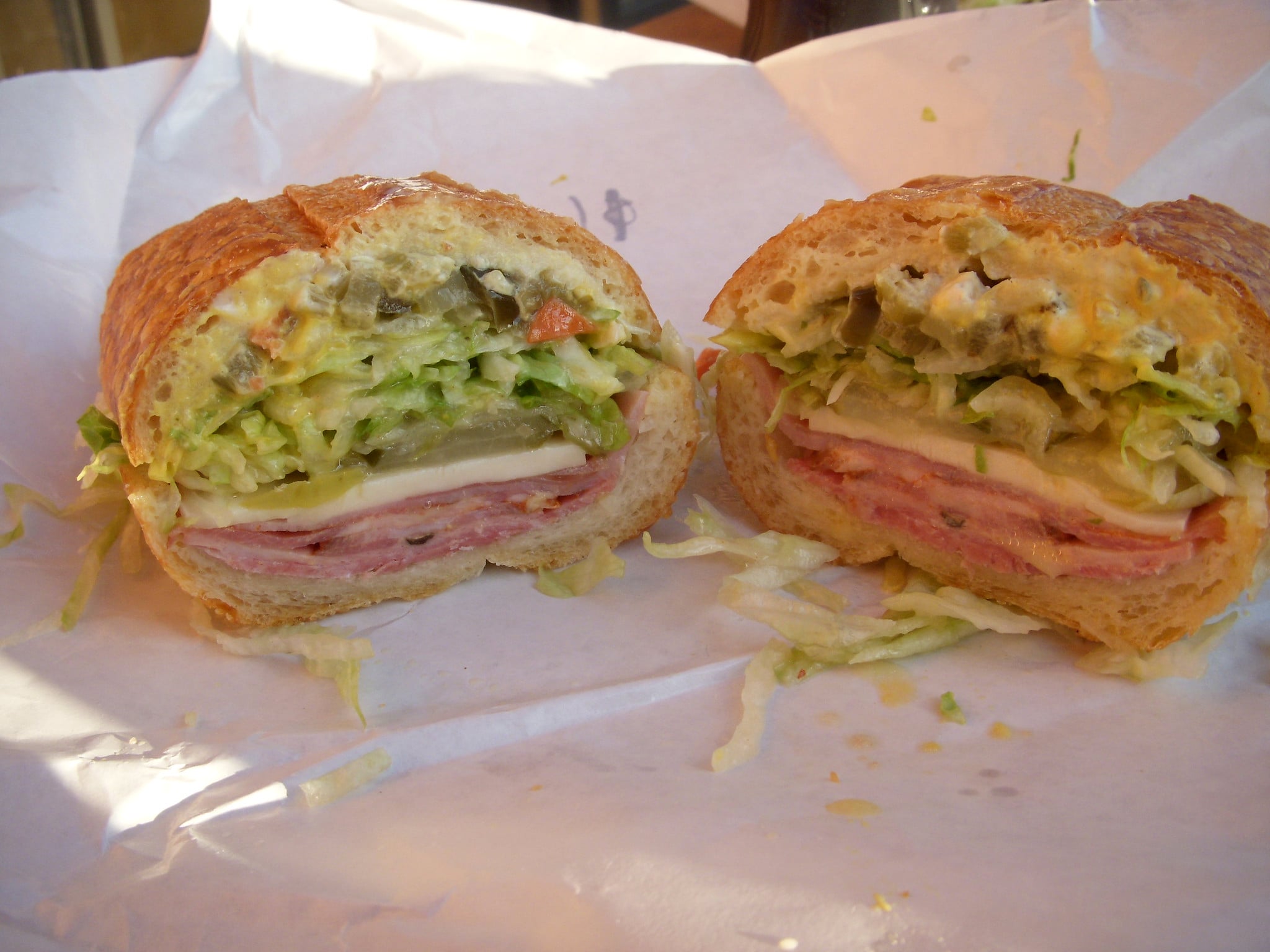 A submarine sandwich cut in half, featuring layers of sliced deli meat, cheese, lettuce, and chopped pickles on a crusty roll.