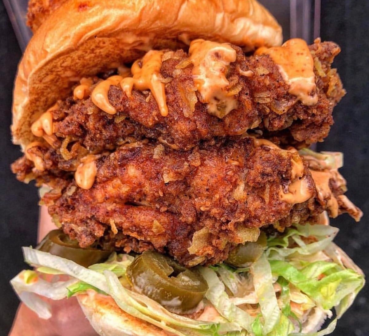 Double fried chicken sandwich with sauce, sliced jalapeños, and shredded lettuce on a bun.