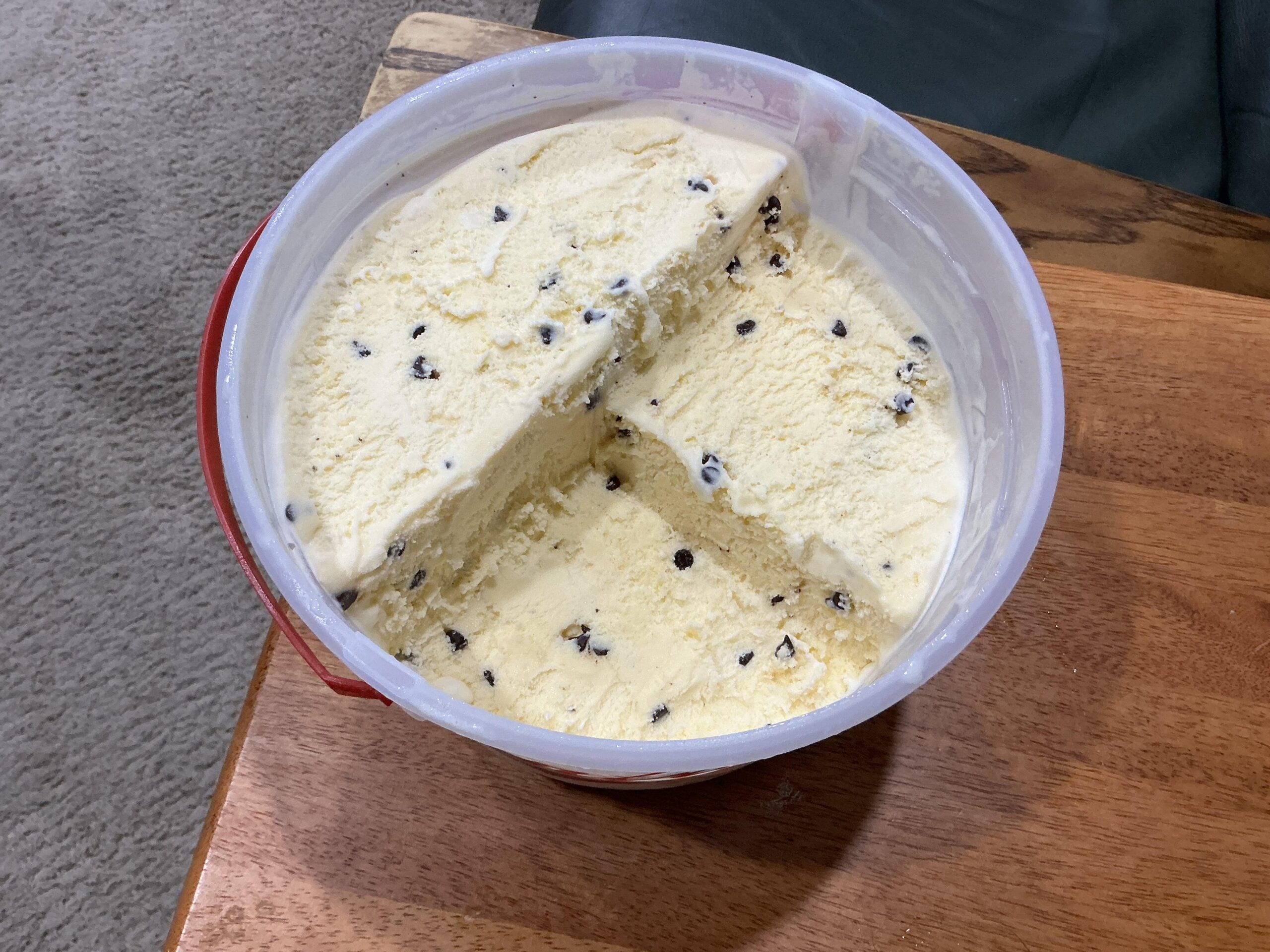 A plastic tub of vanilla ice cream with chocolate chips, with a large wedge portion removed.