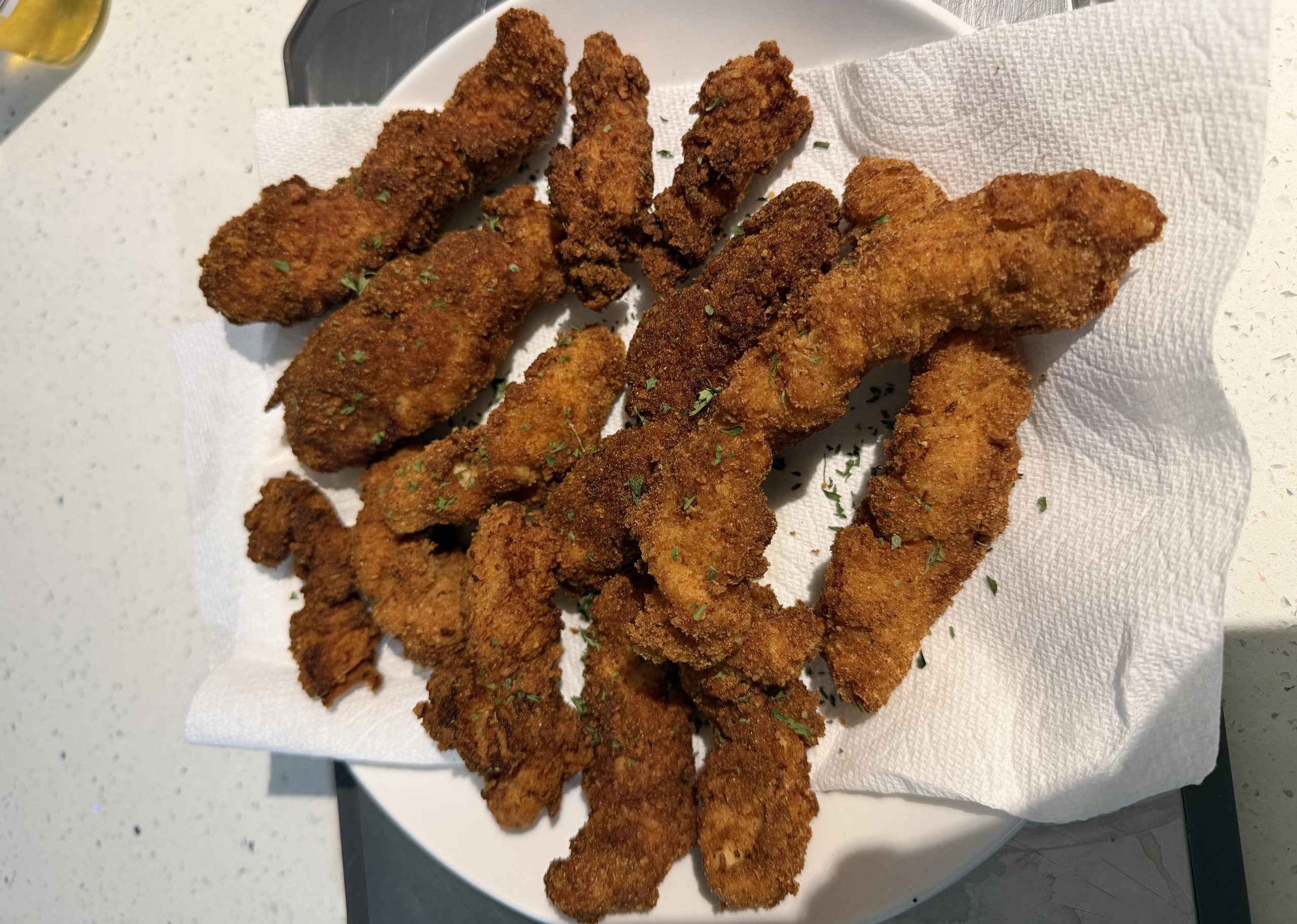 A pile of breaded and fried chicken strips garnished with herbs on a paper towel-lined plate.