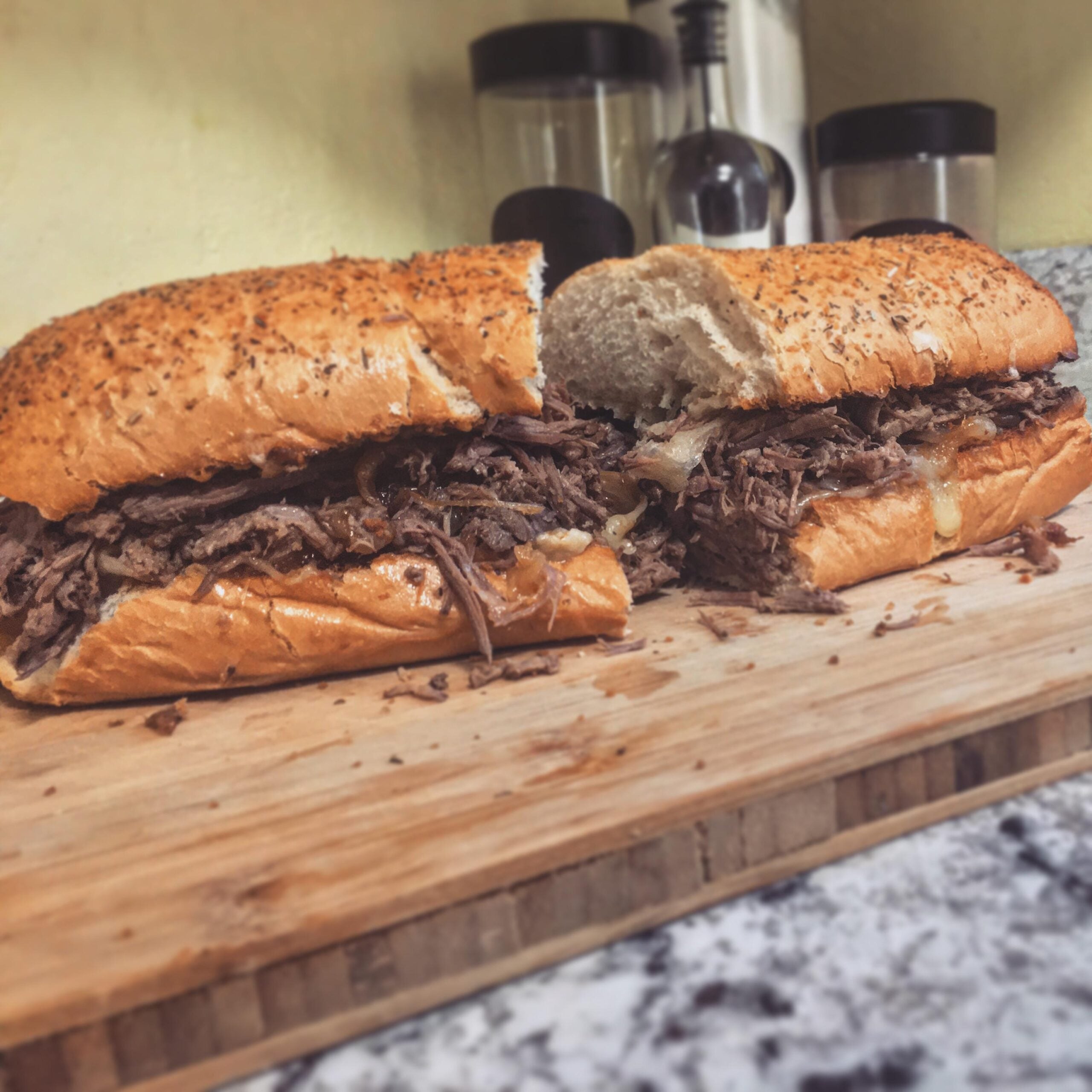 A sliced roast beef sandwich on a toasted hoagie roll resting on a wooden cutting board.