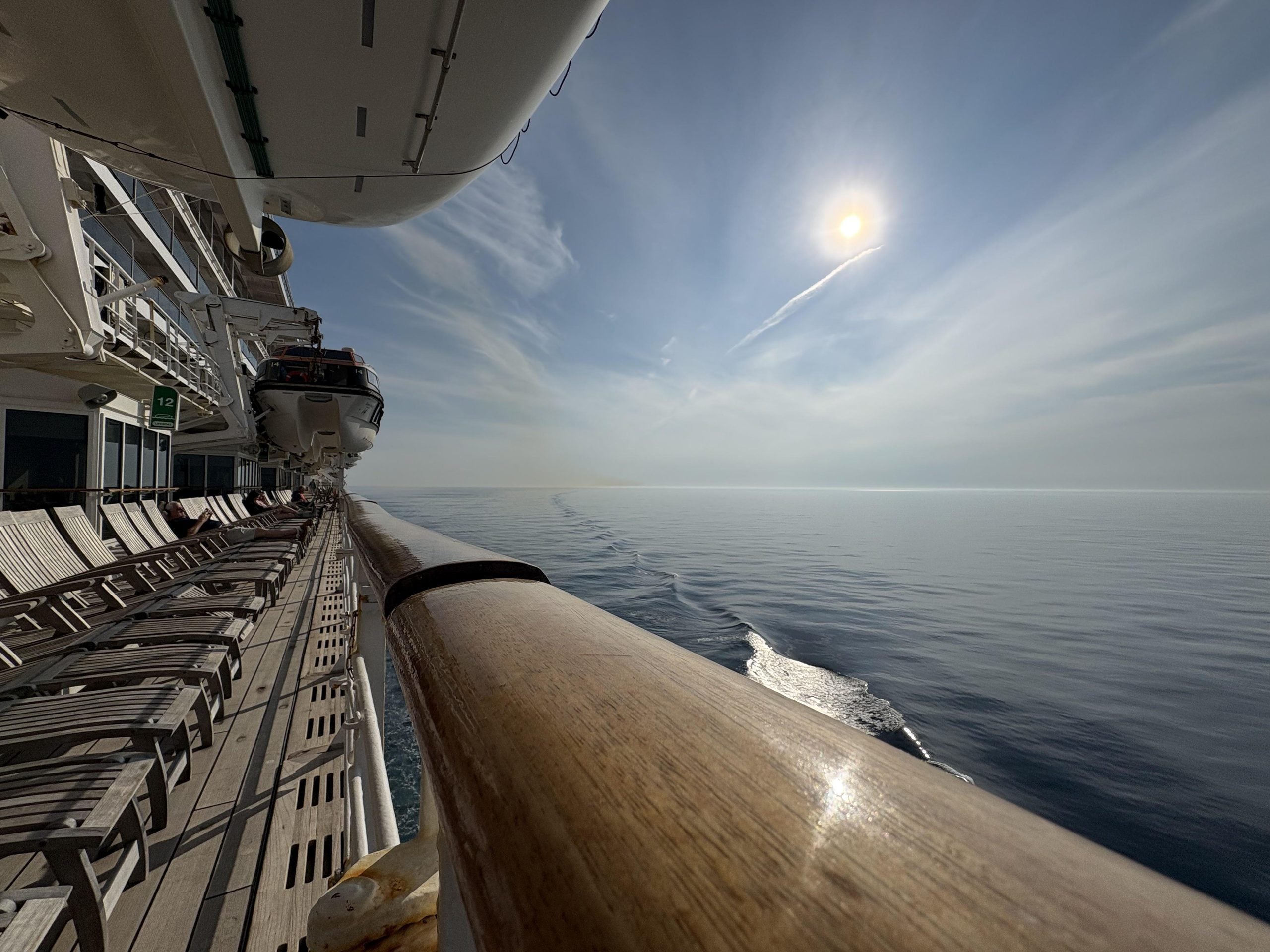 Cruise ship photos: View from the wooden railing of a cruise ship deck looking out over a calm ocean under a sunny sky.