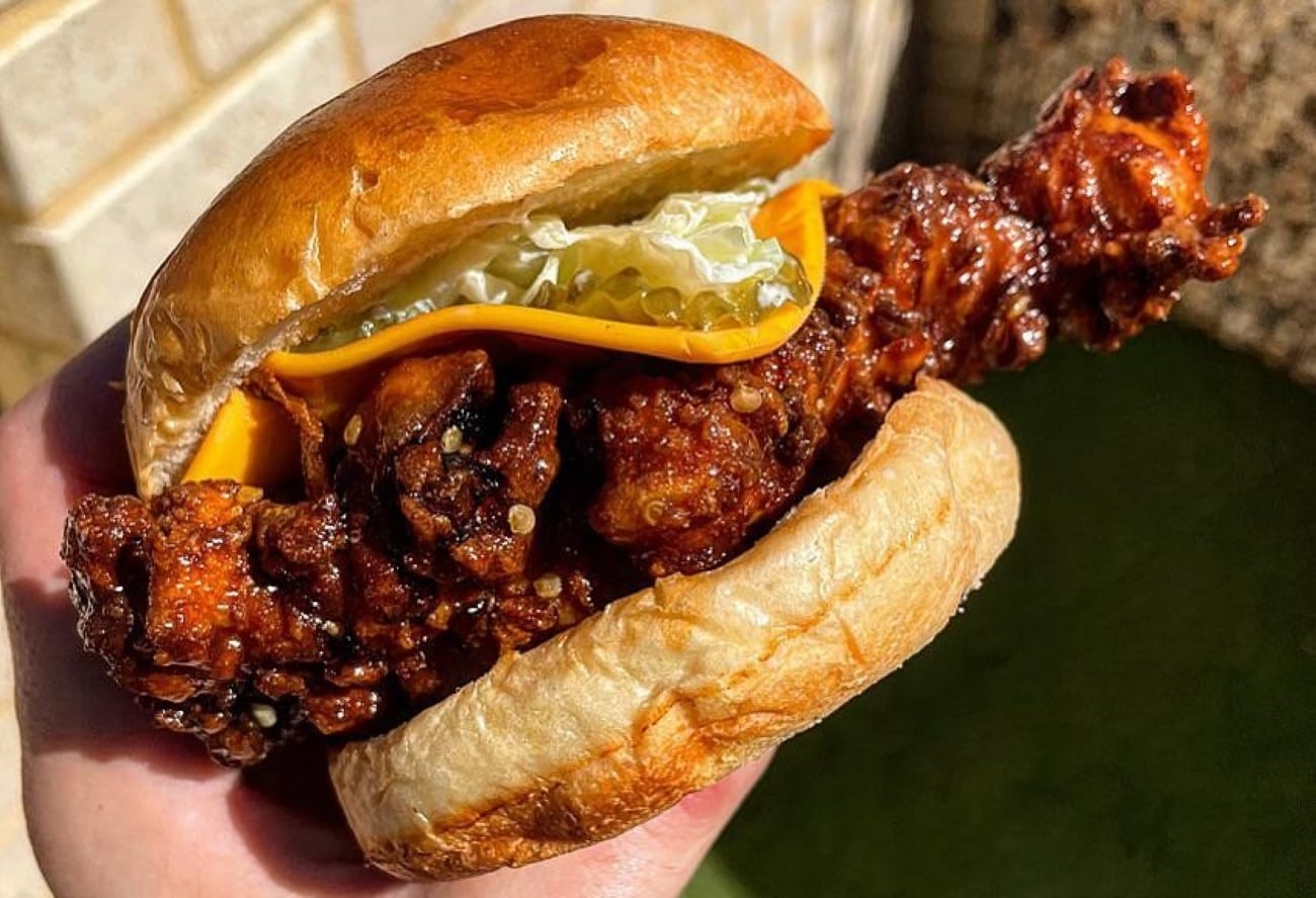 A fried chicken sandwich on a bun with melted cheese and pickles, held in a hand.