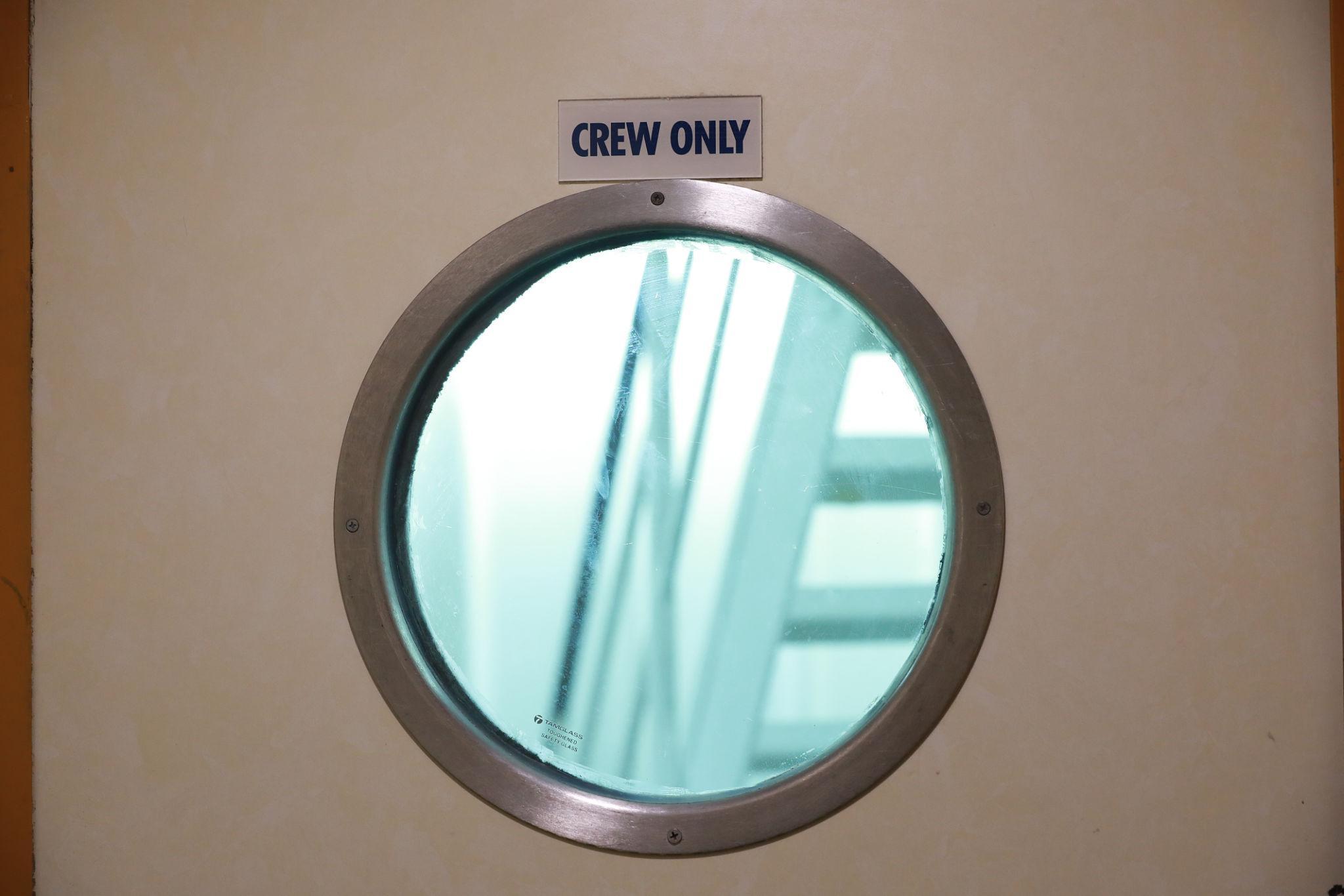 A door with a circular window and a sign above that reads “CREW ONLY.”