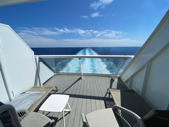 View of the ocean wake from a cruise ship balcony featuring two lounge chairs and a small table.