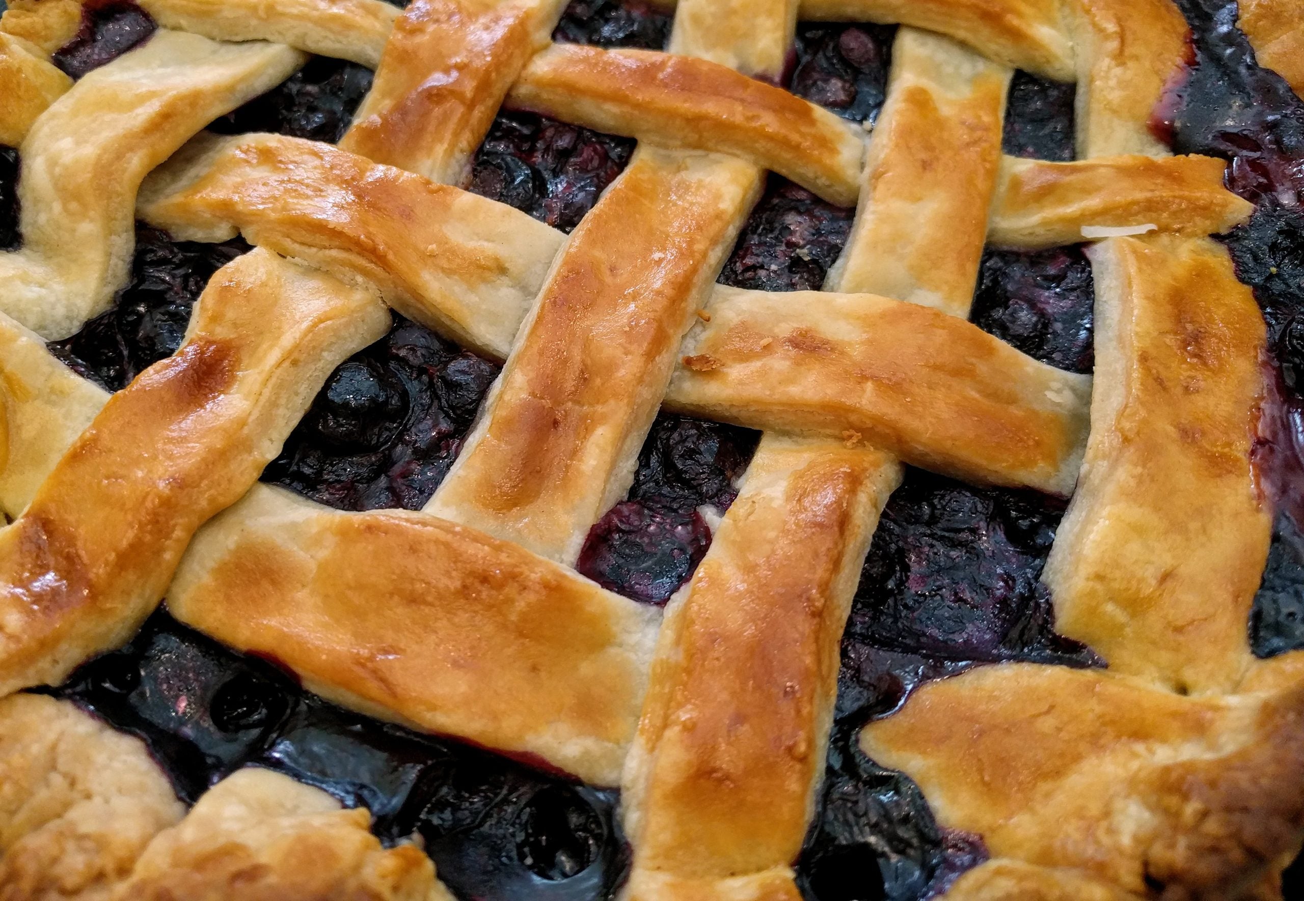 A close-up of a blueberry regional dessert pie with a golden-brown lattice crust.
