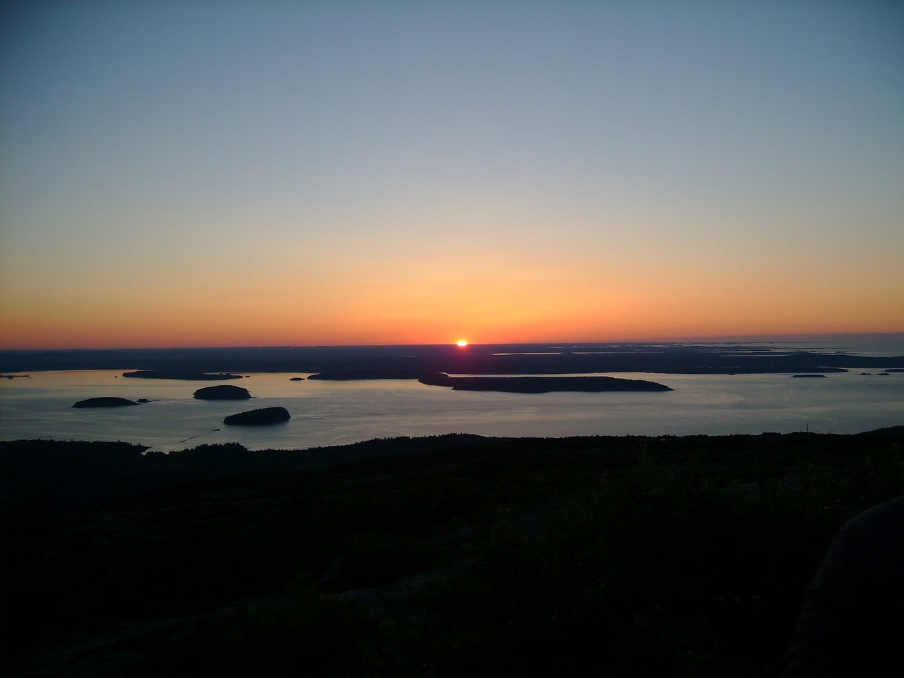 The sun setting over a coastal landscape with several small islands in the water.