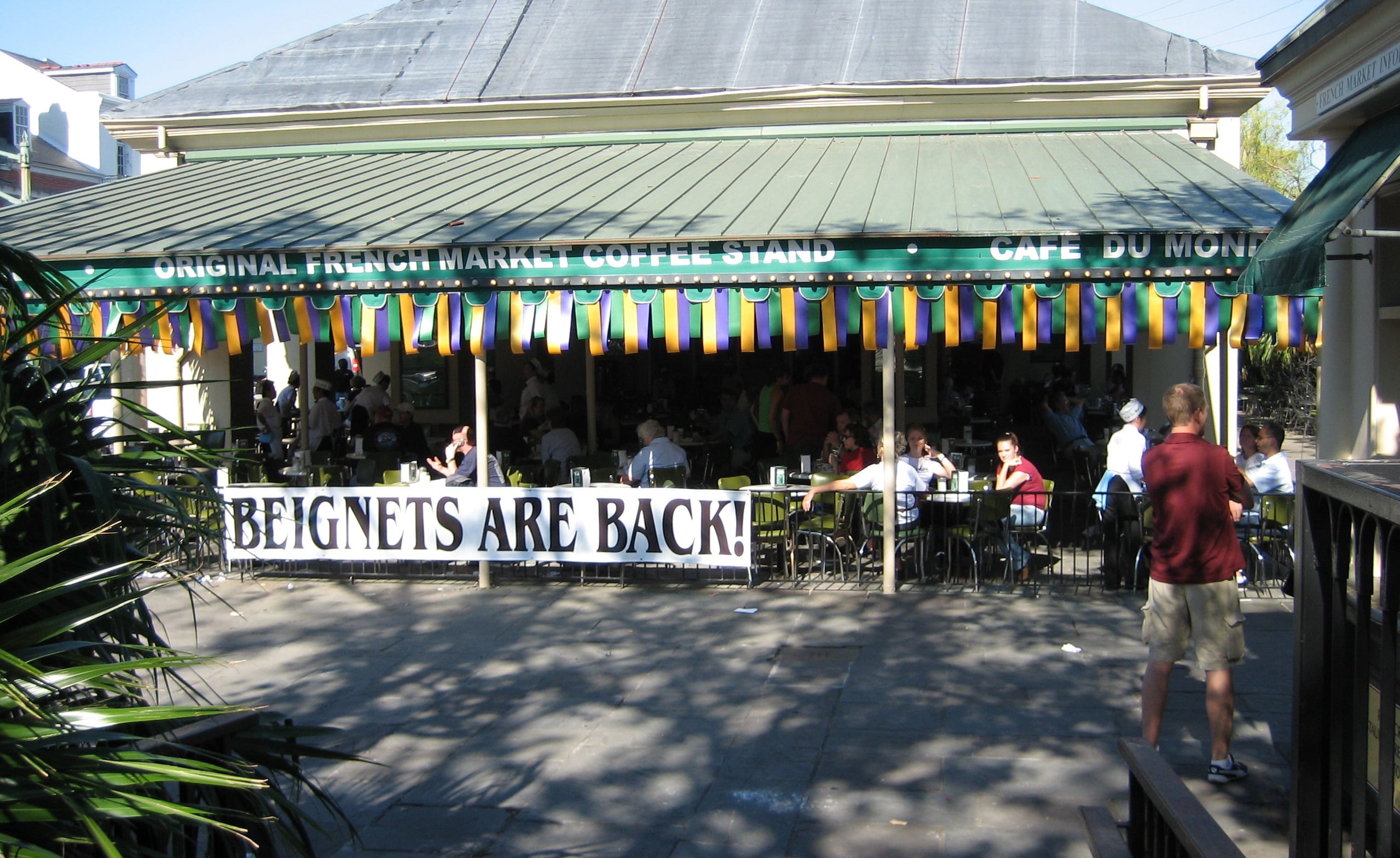 Cafe Du Monde in the French Market with a banner that reads “BEIGNETS ARE BACK!” hanging in front of seated patrons.