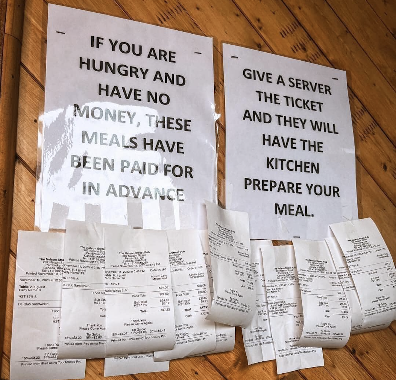 Two signs explain that meals are prepaid for those in need; beneath them are numerous meal tickets attached to a wooden wall, ready for servers to use.