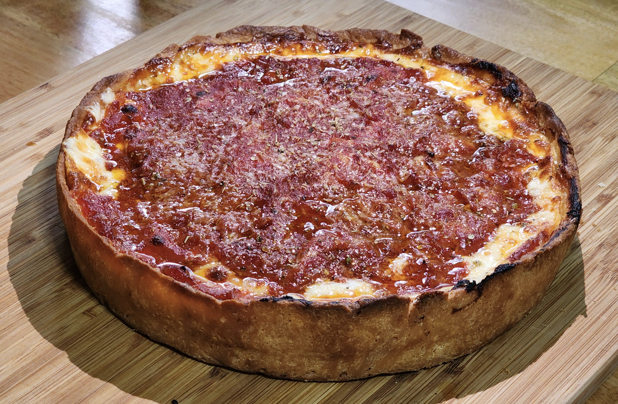 A whole Chicago-style deep dish pizza topped with tomato sauce sits on a wooden cutting board. The thick, golden crust and melted cheese edge are visible under the layer of sauce.