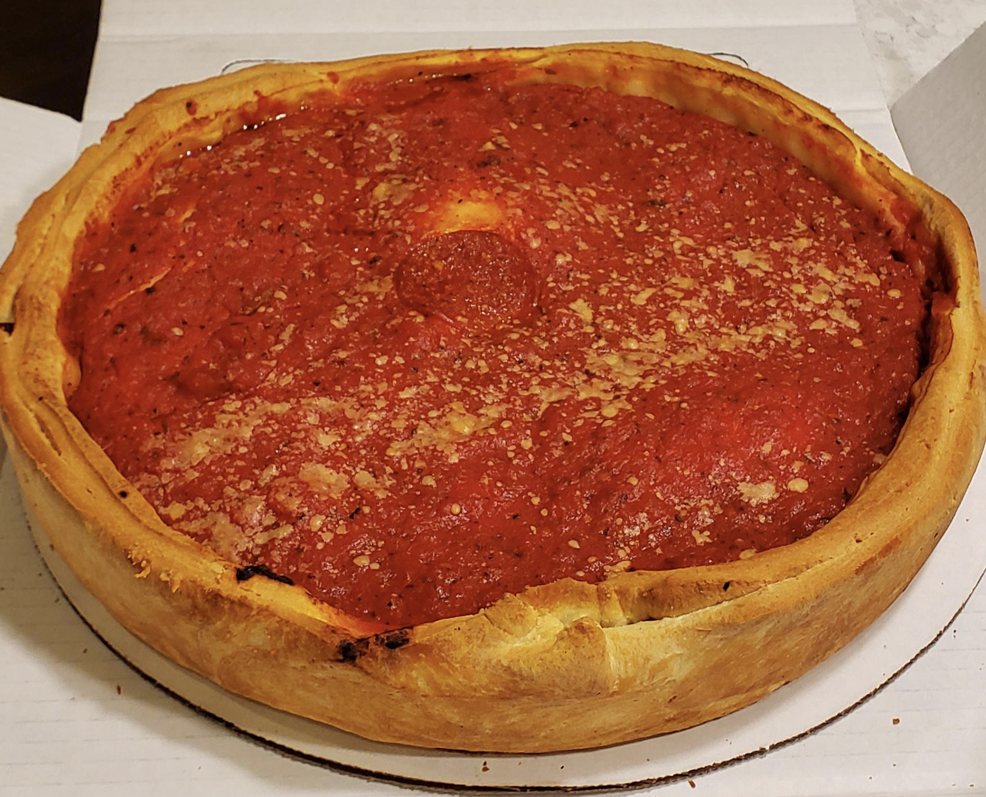 A whole Chicago-style deep-dish pizza with a thick golden crust, topped with chunky tomato sauce and sprinkled with grated cheese, sits in an open pizza box.