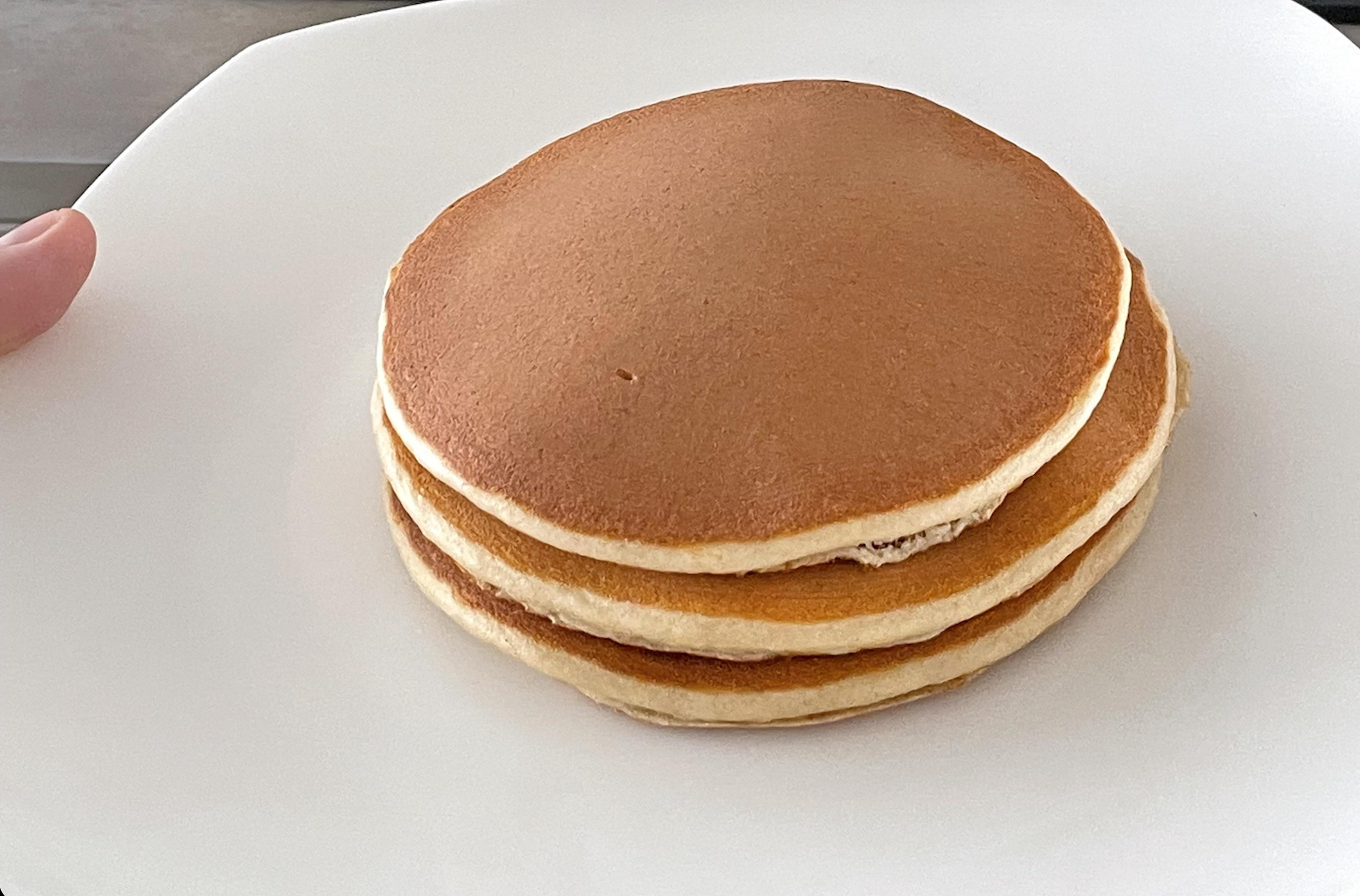 A stack of three golden-brown pancakes on a white plate.