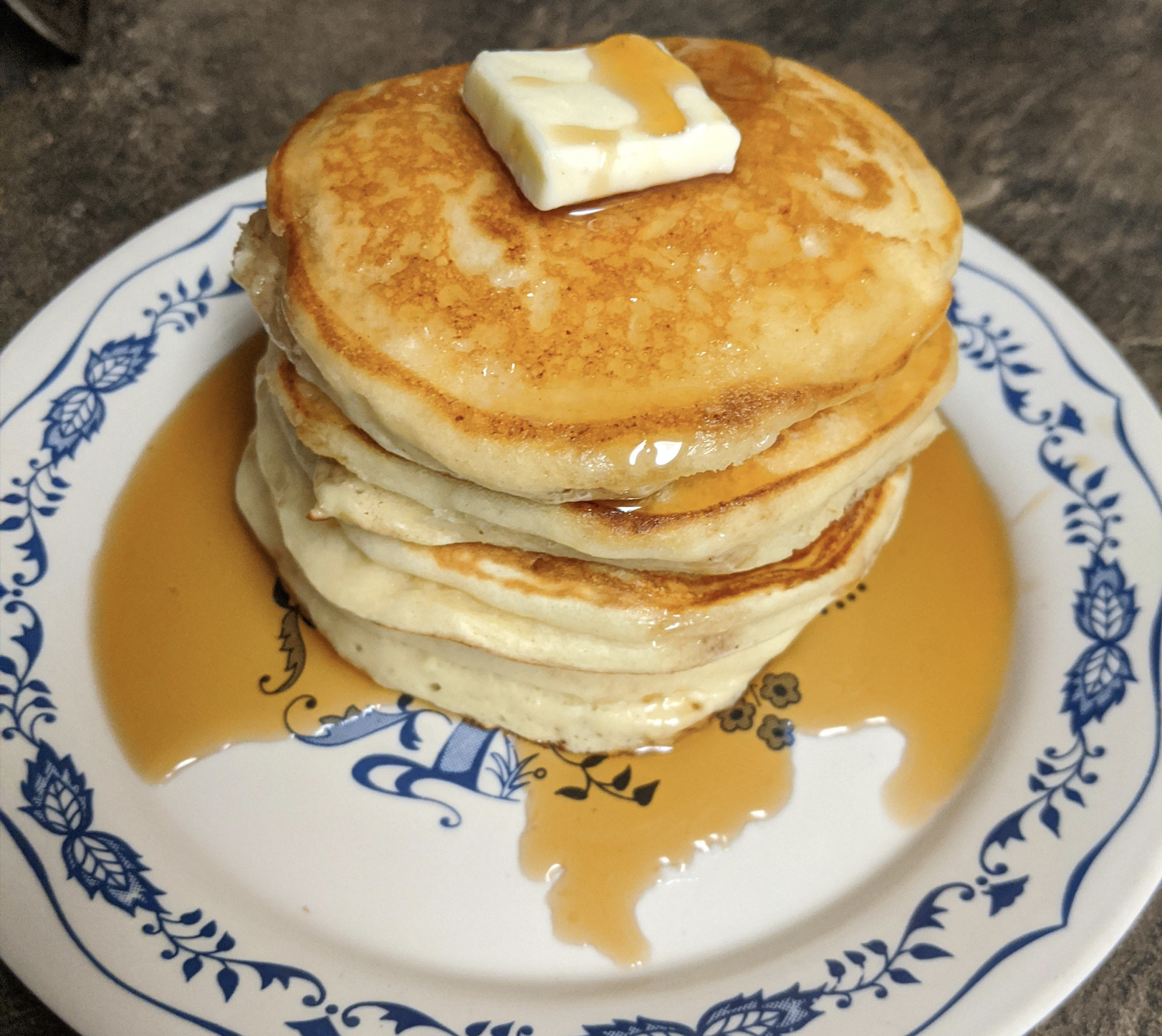A stack of pancakes topped with a pat of butter and syrup on a blue and white patterned plate.