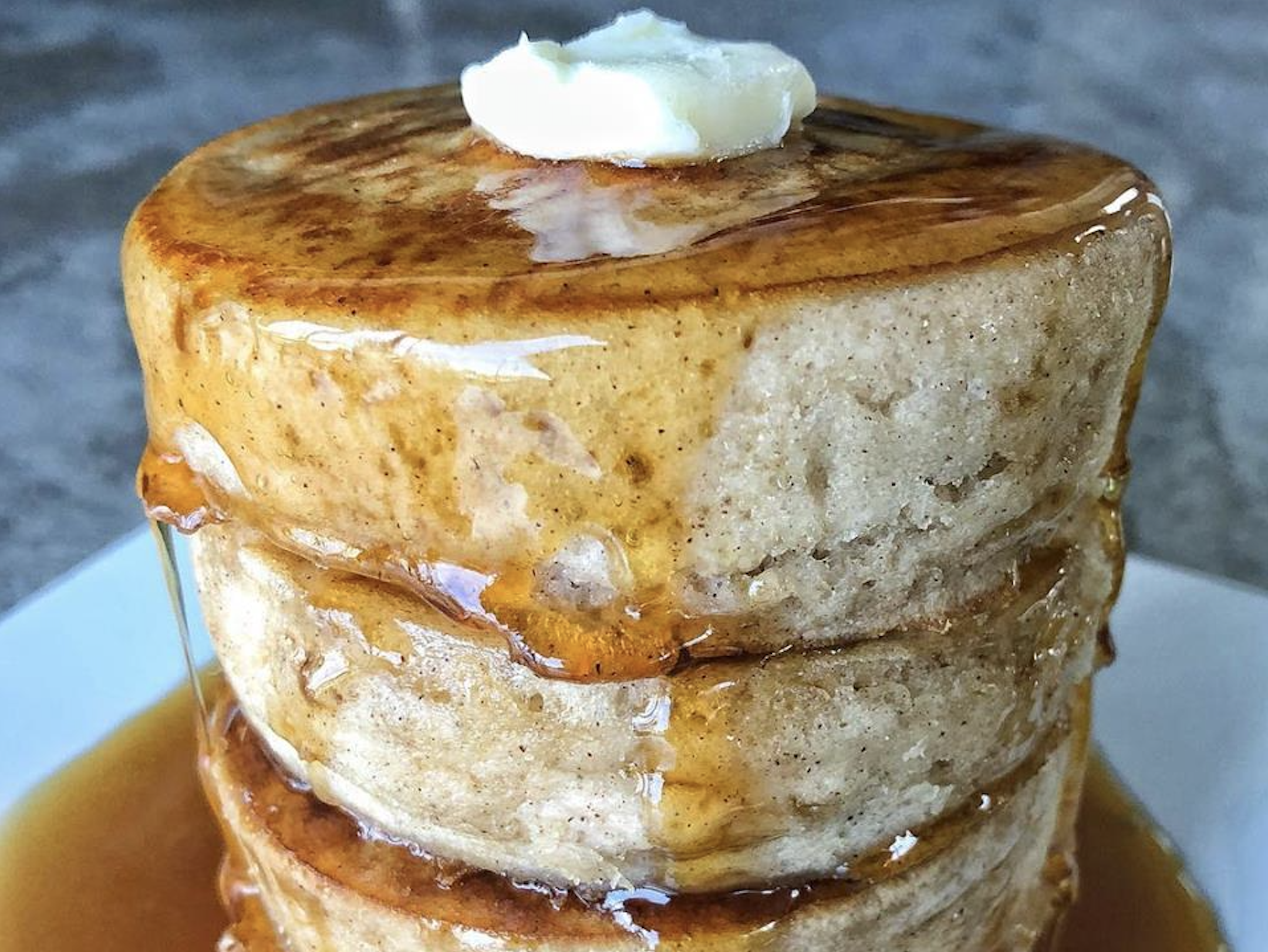 A stack of three thick pancakes topped with a pat of melting butter and drizzled with syrup.