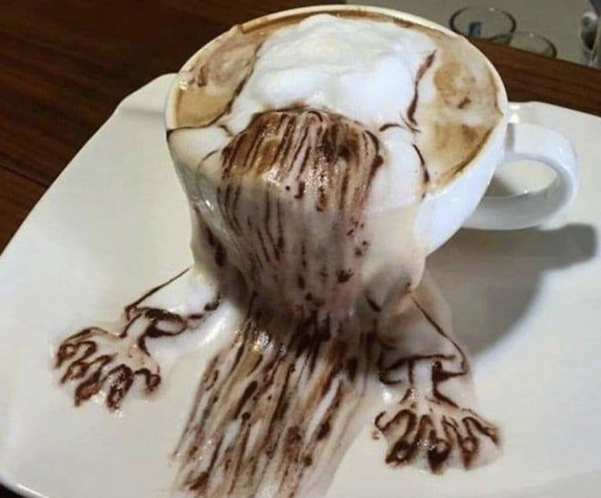 A cup of coffee with foam art designed to look like a waterfall spilling over the edge and onto the saucer.