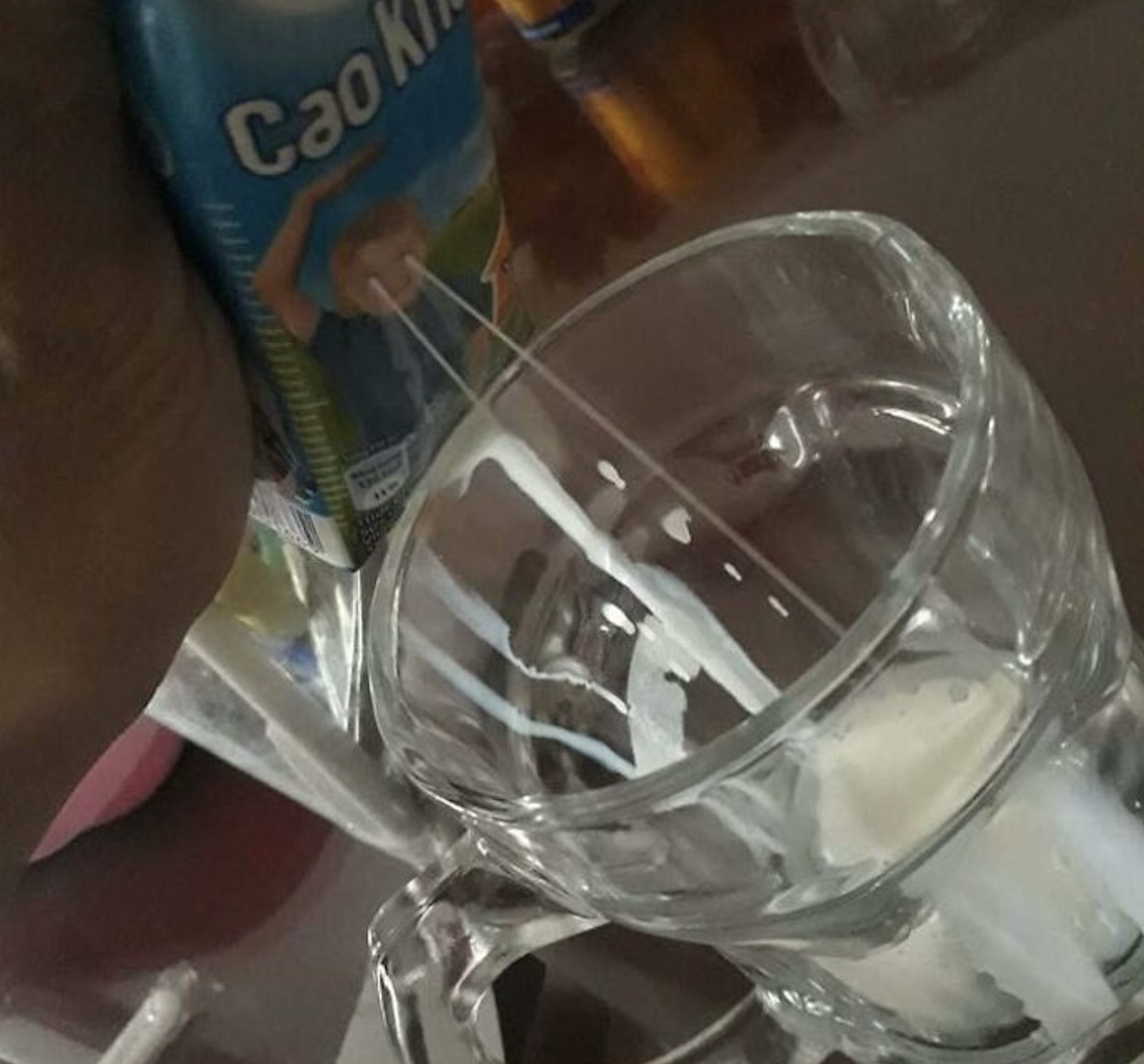 A hand pouring white liquid from a Cao Kiu beverage carton into a glass mug.