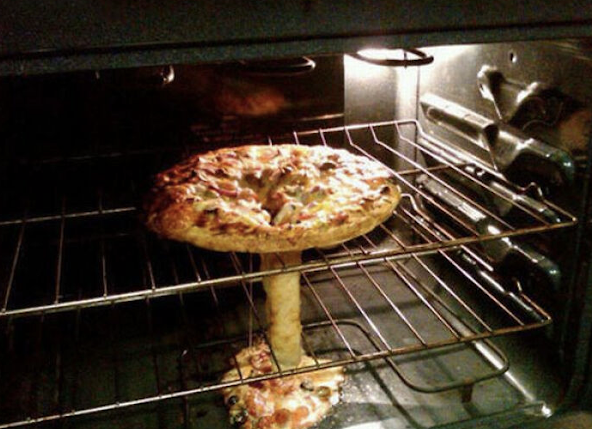 A pizza balanced on a vertical crust column in an oven, resembling a mushroom cloud.