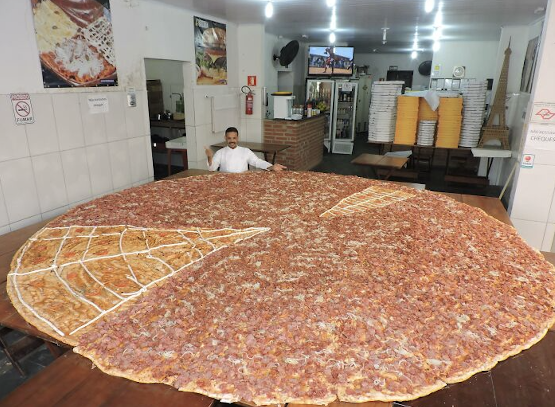 A man stands behind an oversized, round pizza that covers a large table in a restaurant.