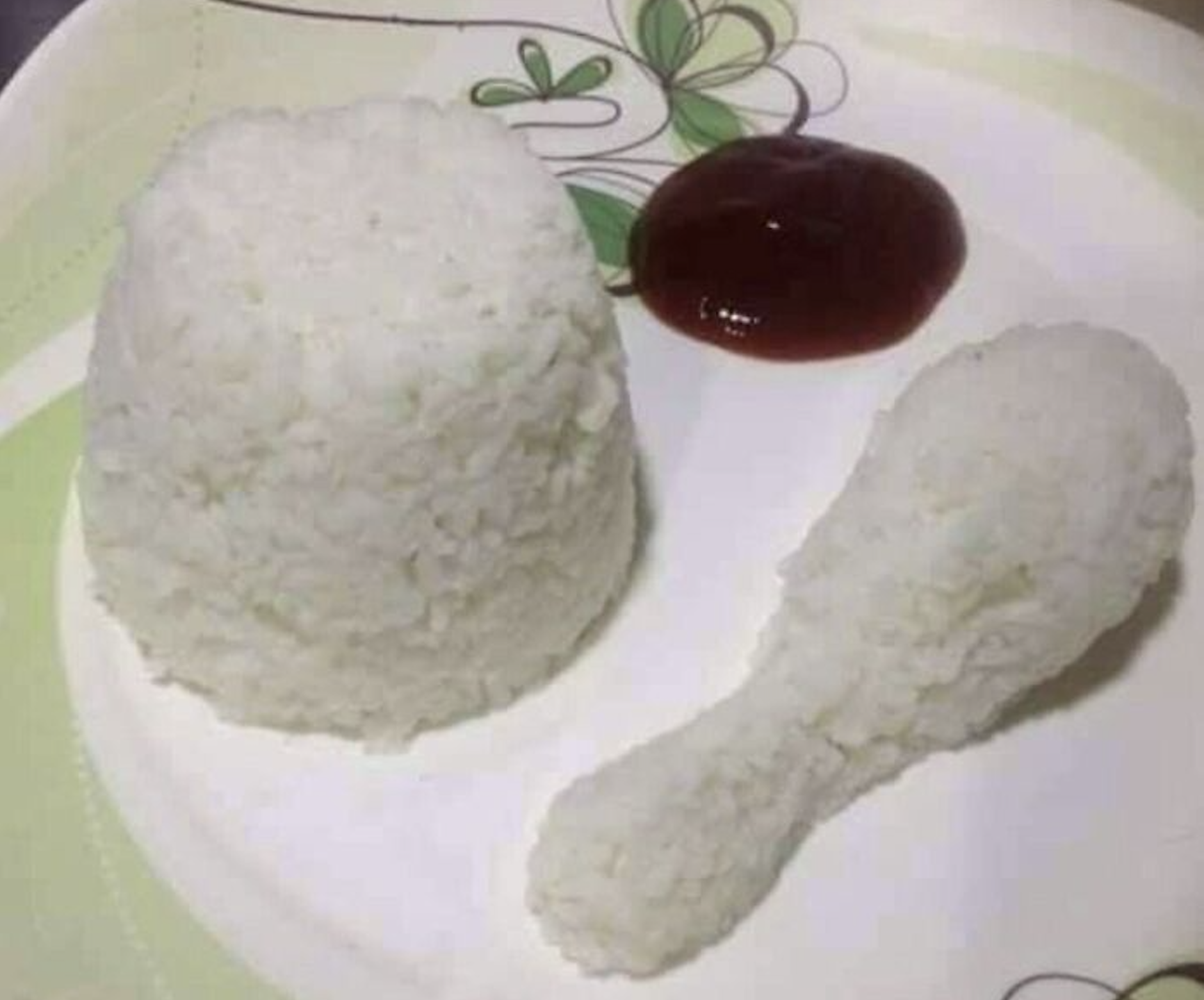 A molded mound of white rice next to a drumstick-shaped portion of rice and a small dollop of red sauce on a plate.