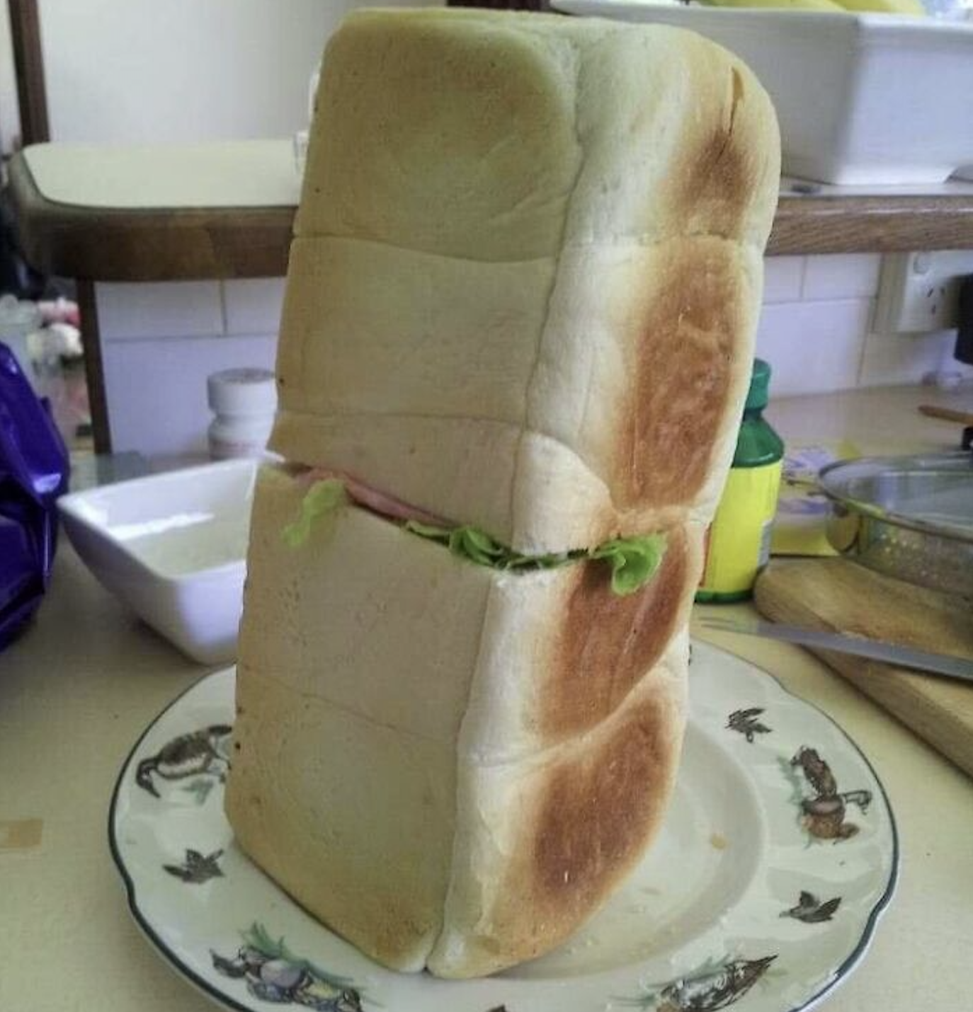 A tall, vertical sandwich made of two thick blocks of white bread with lettuce and ham visible in the middle, resting on a patterned plate.