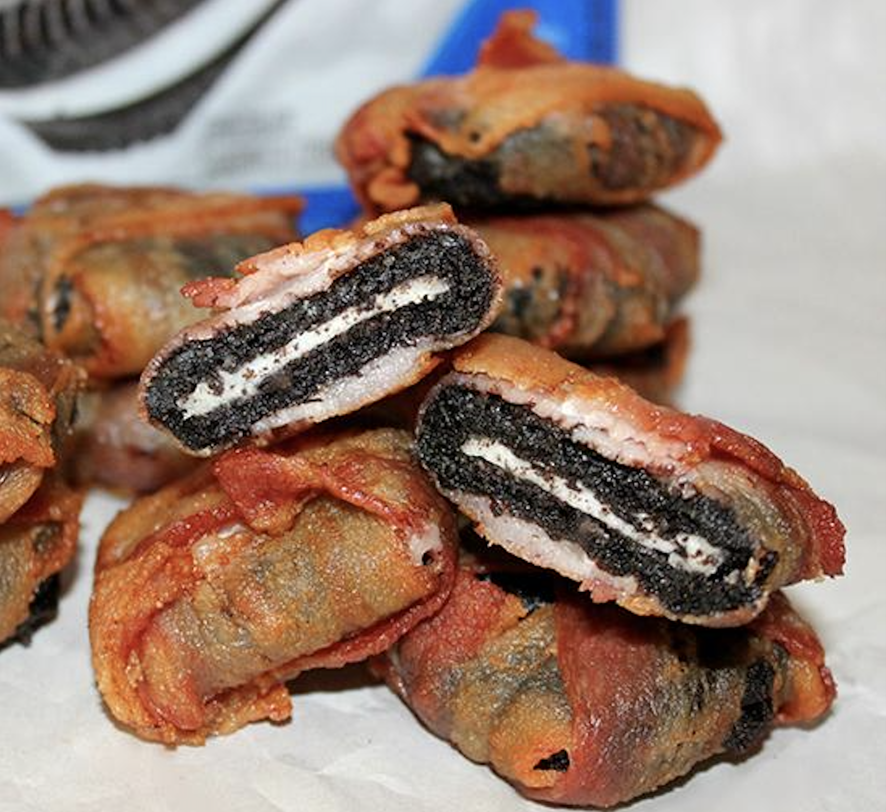 A pile of Oreo cookies wrapped in bacon, with two cookies sliced in half to show the cream filling.