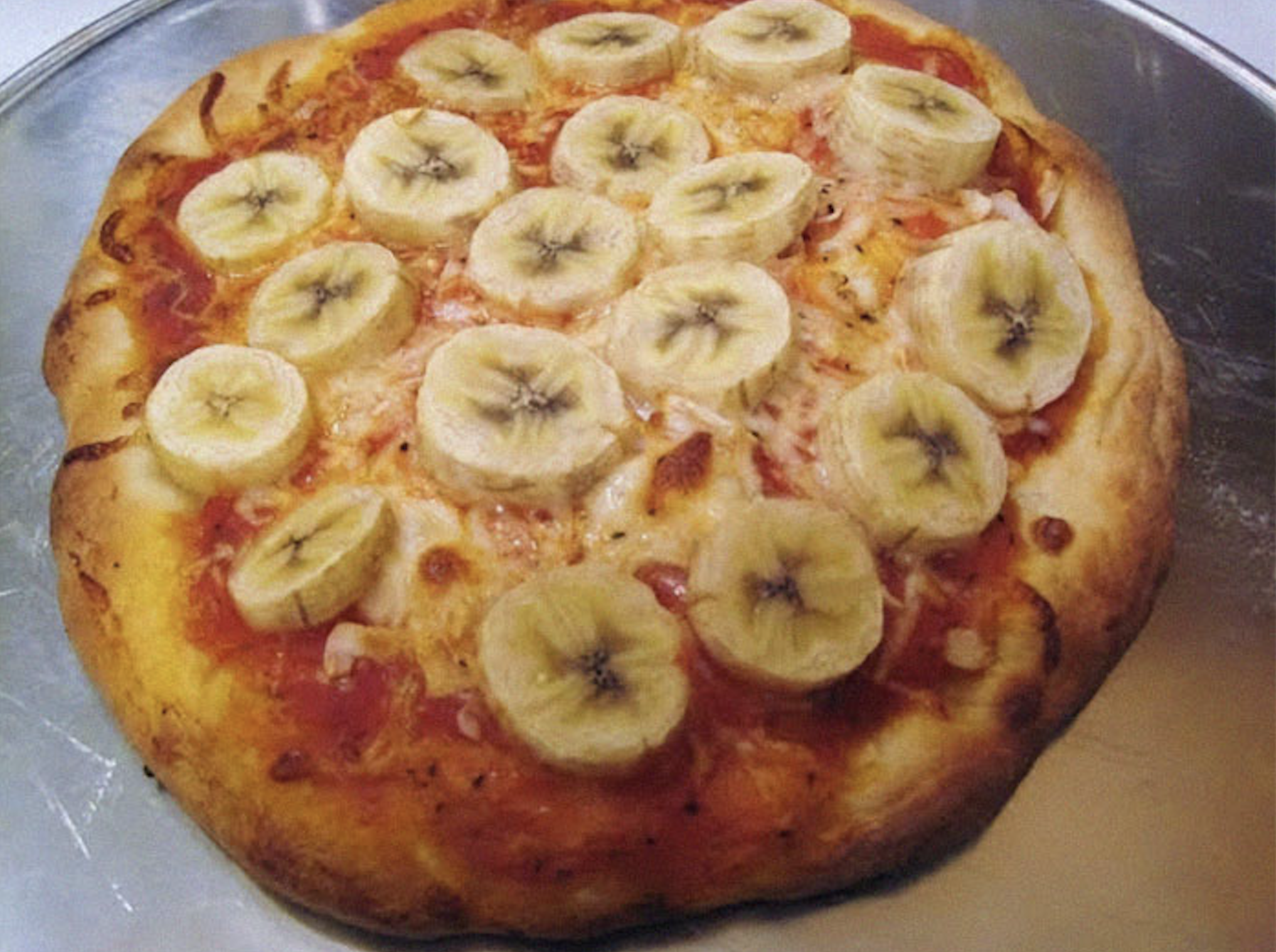 A baked pizza topped with tomato sauce, melted cheese, and sliced bananas.