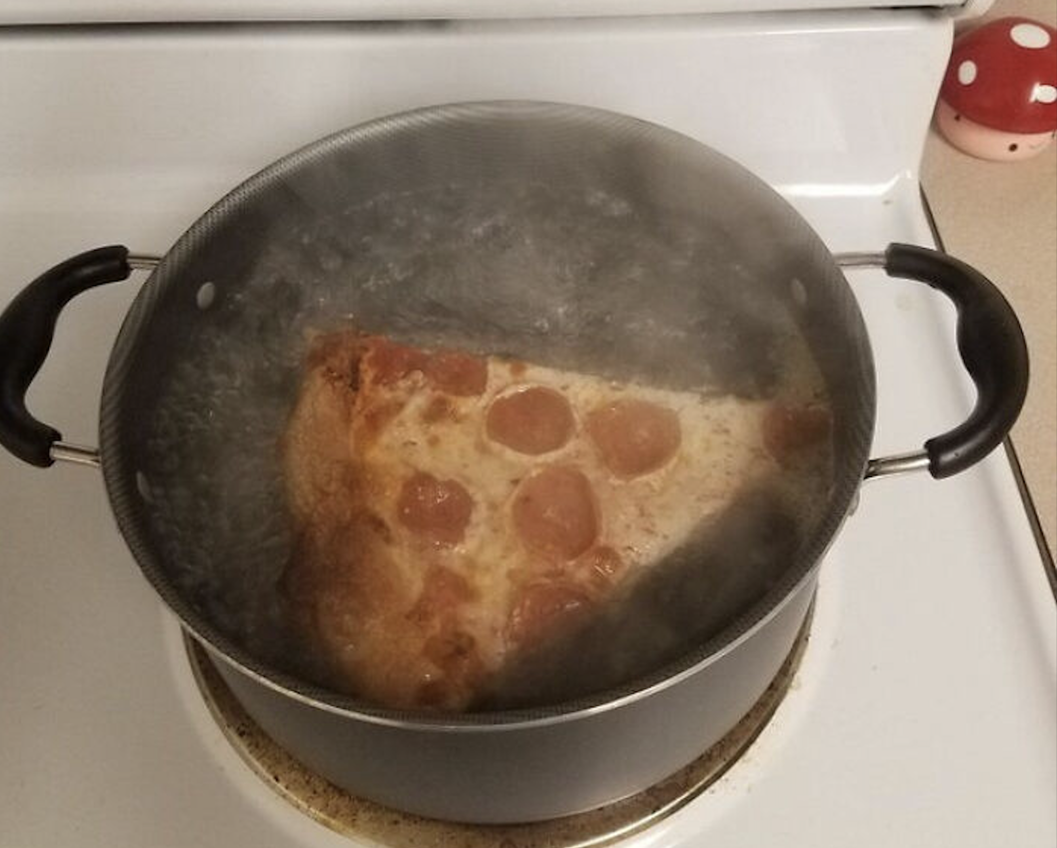 A slice of pepperoni pizza boiling in a pot of water on a stovetop.