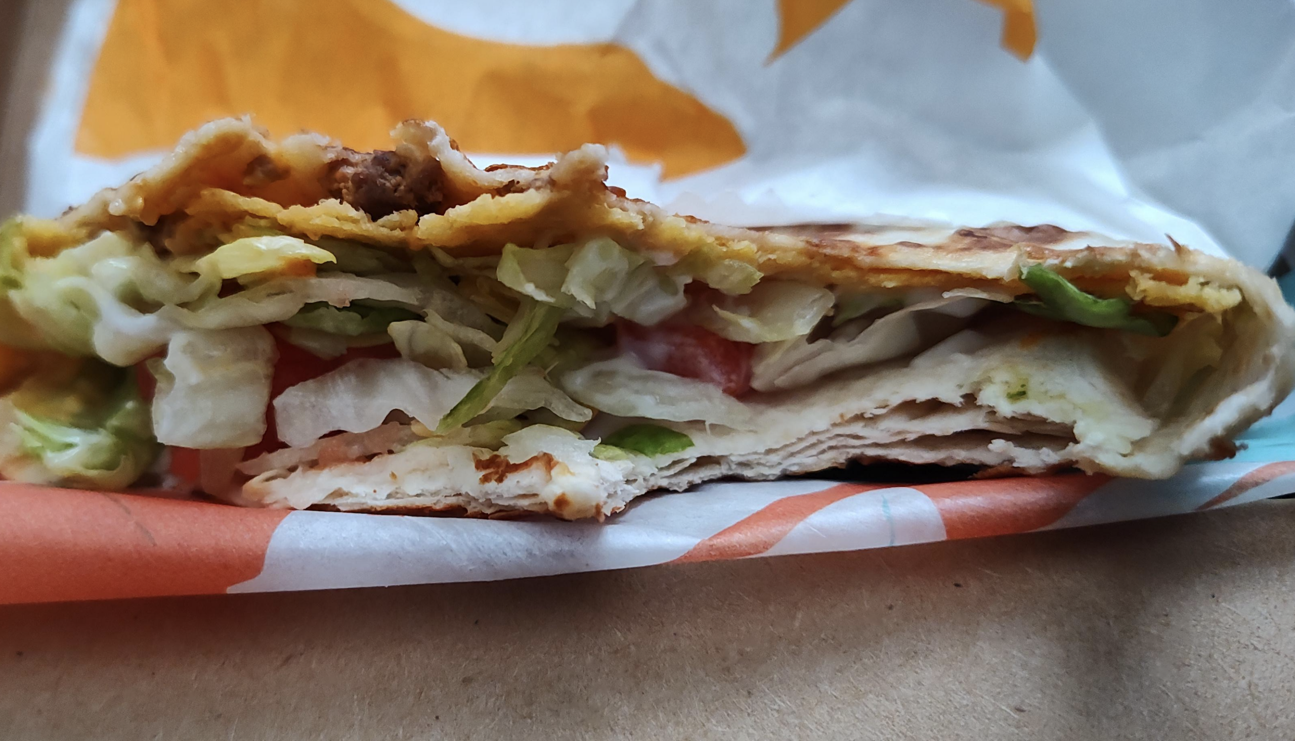 A folded tortilla sandwich filled with lettuce, tomato, and seasoned meat, resting on a fast-food wrapper.
