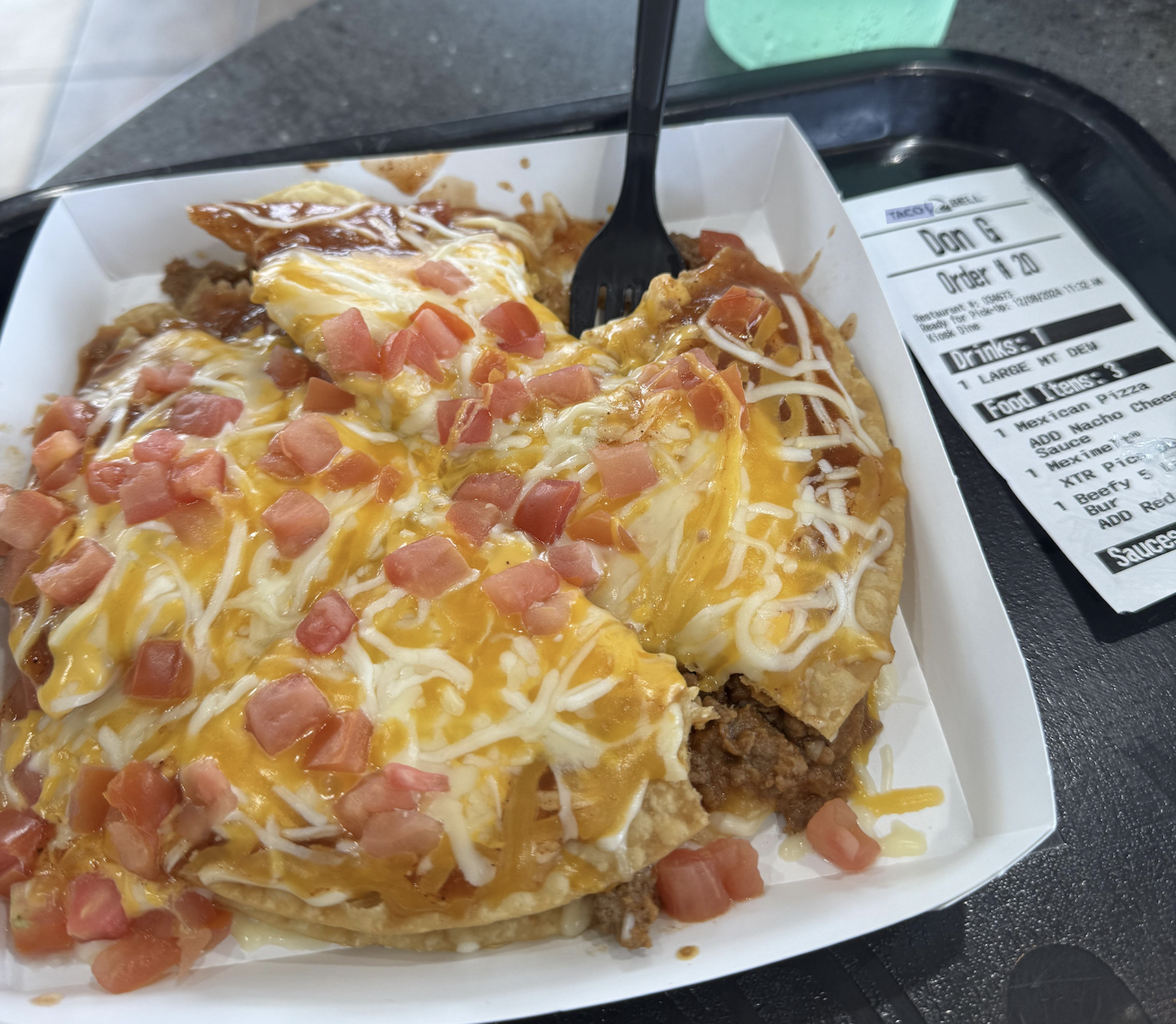 Taco Bell Mexican Pizza topped with melted cheese and diced tomatoes in a white tray next to a paper receipt.