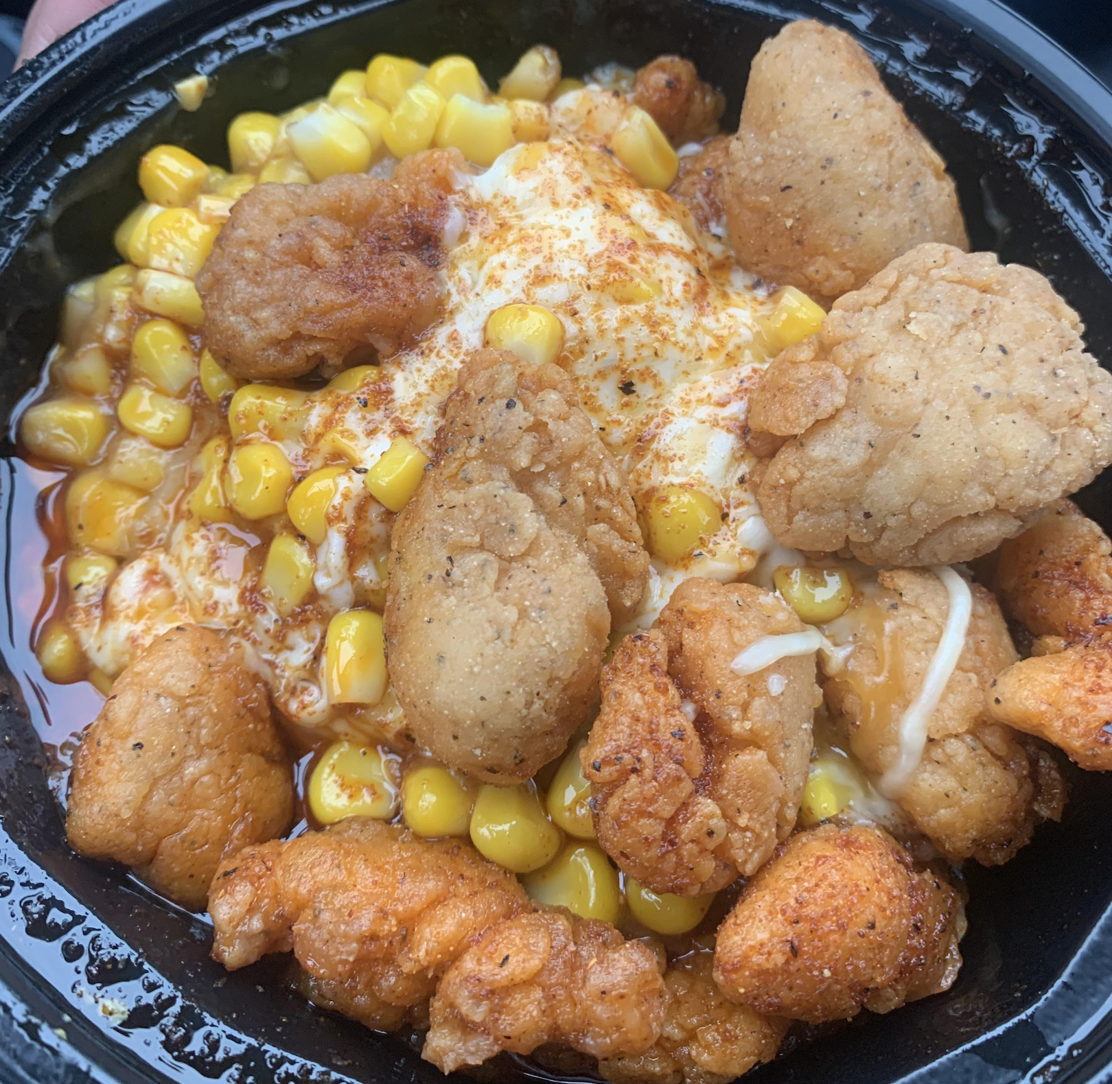 A bowl of corn topped with fried chicken nuggets, melted cheese, and a dusting of seasoning.