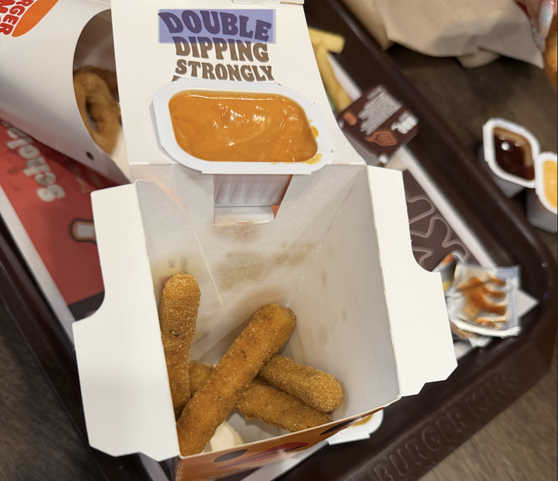 A Burger King box containing mozzarella sticks with a dipping sauce cup attached to the open lid.