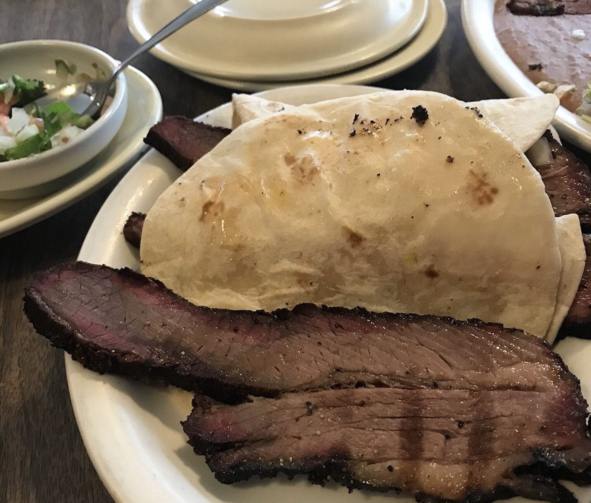 Slices of grilled brisket served with flour tortillas, accompanied by a small bowl of pico de gallo.