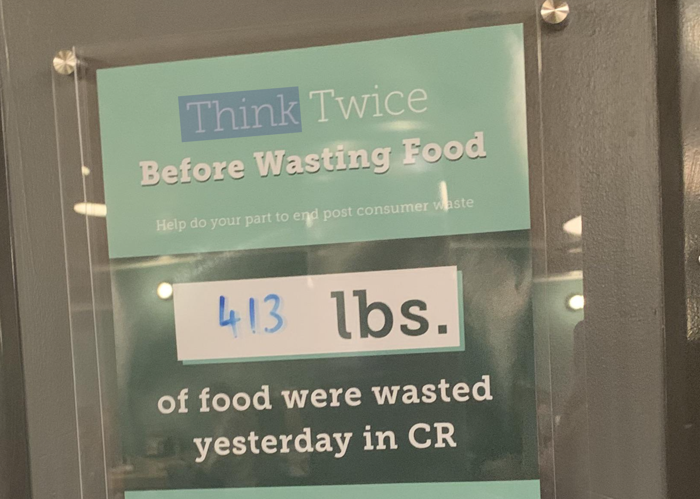 Sign reading “Think Twice Before Wasting Food. Help do your part to end post consumer waste. 413 lbs. of food were wasted yesterday in CR.”