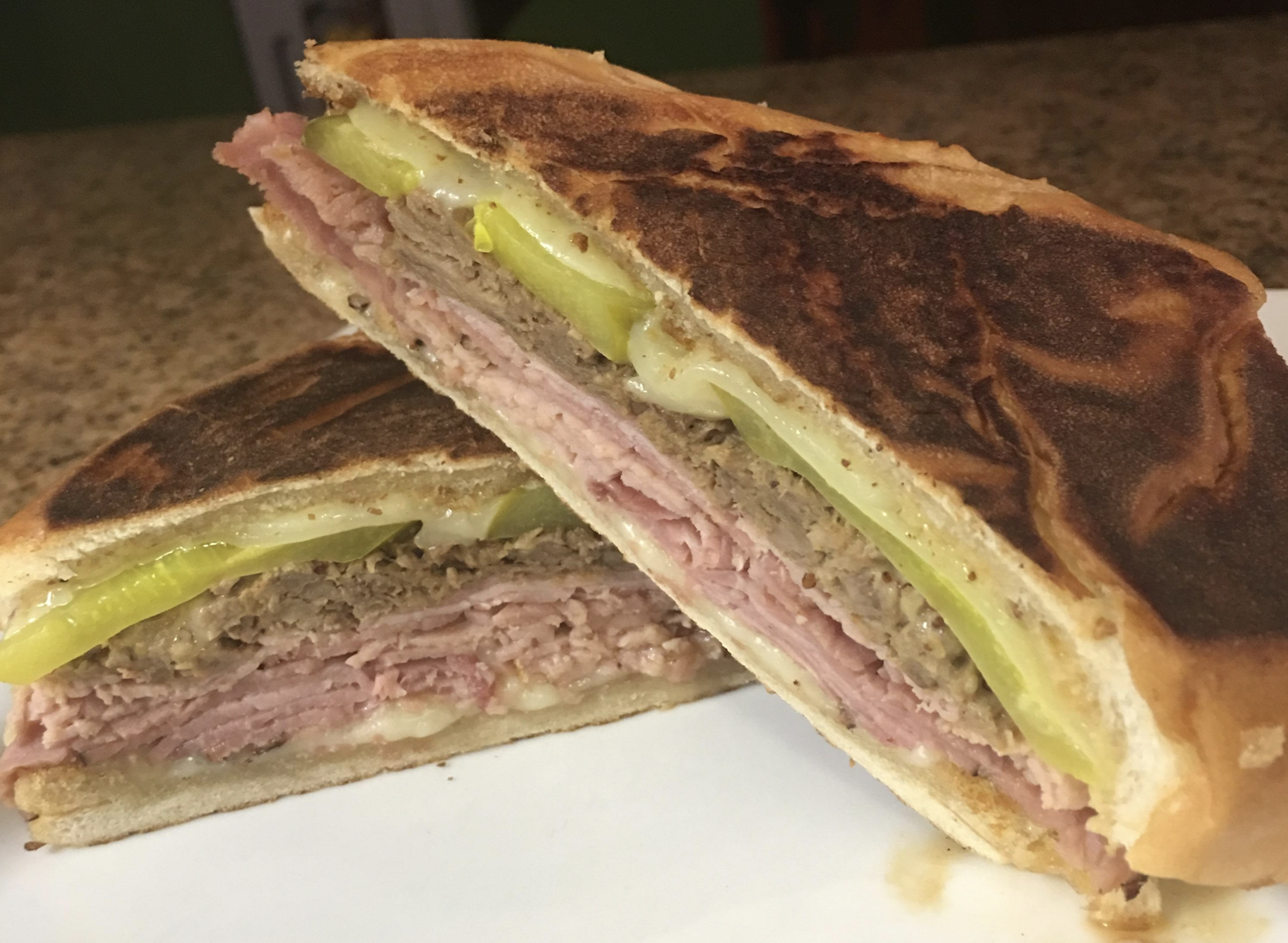A pressed Cuban sandwich cut in half, showing layers of ham, roasted pork, swiss cheese, and pickles on toasted bread.