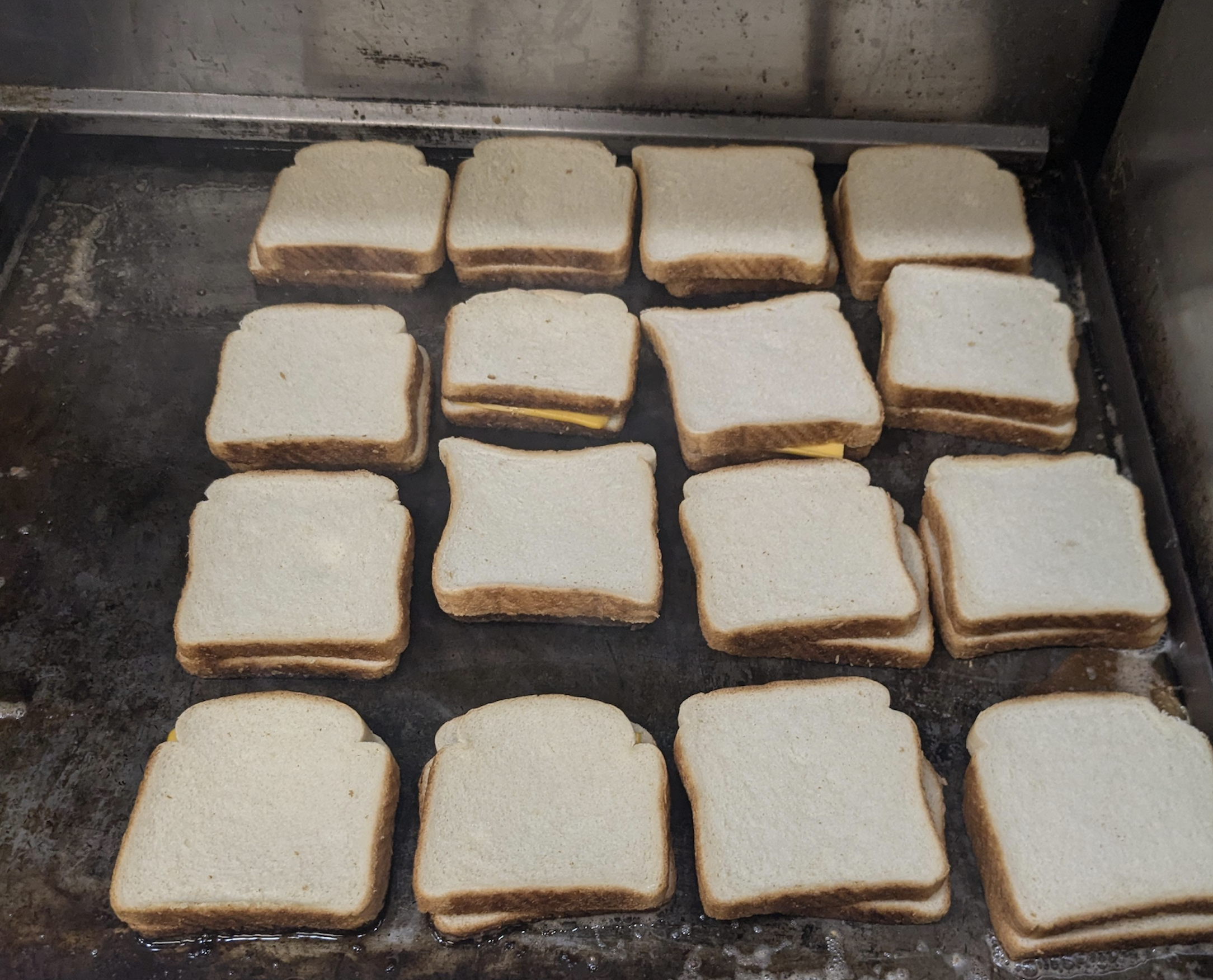 Multiple grilled cheese sandwiches cooking on a flat-top grill.