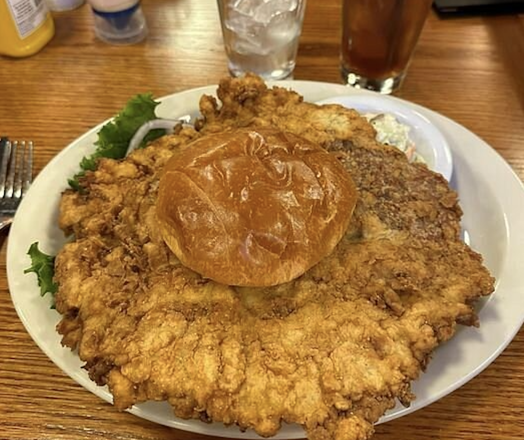 A large breaded pork tenderloin served on a bun on a white plate.