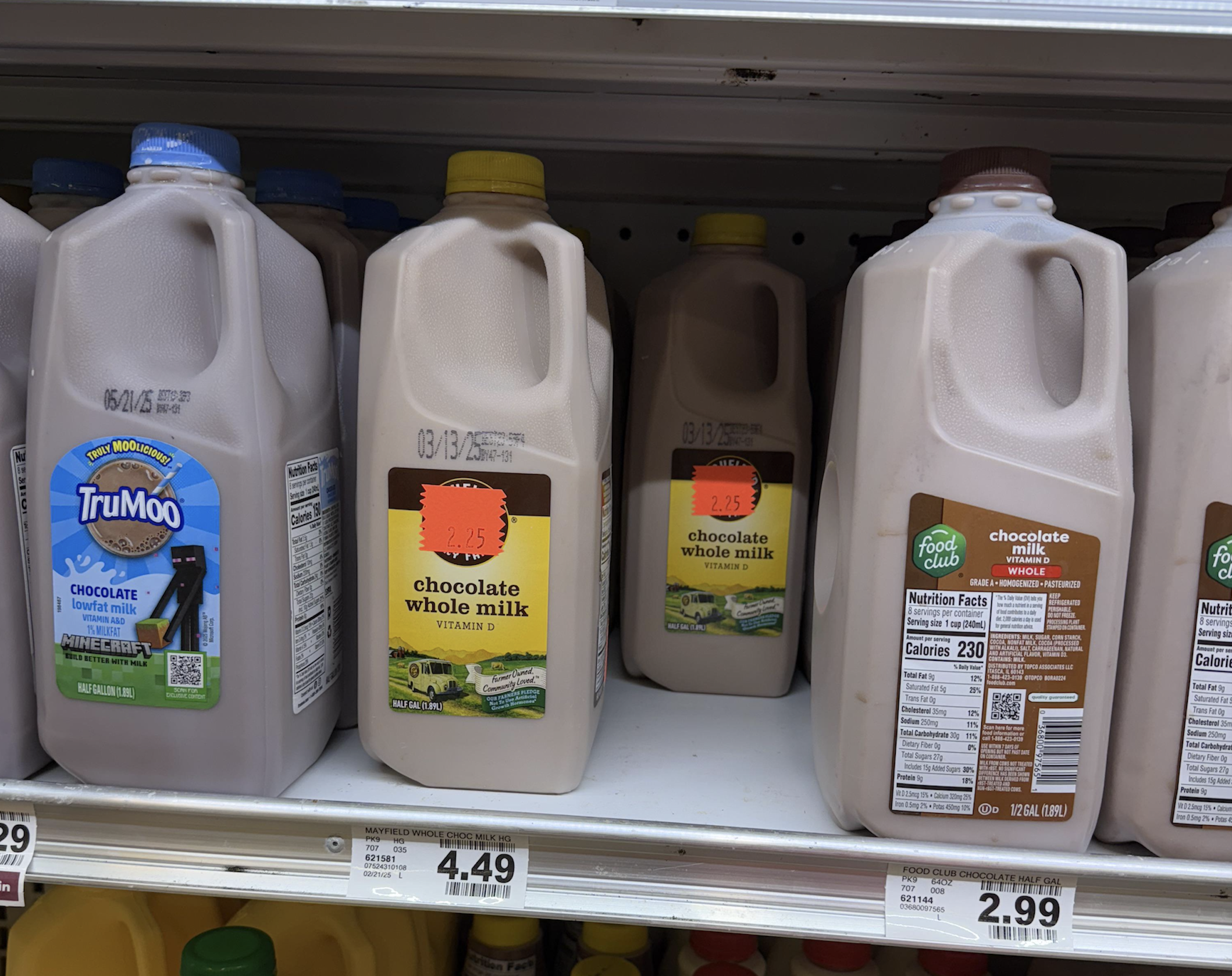 Four half-gallon jugs of chocolate milk on a store shelf, including TruMoo and Food Club brands.
