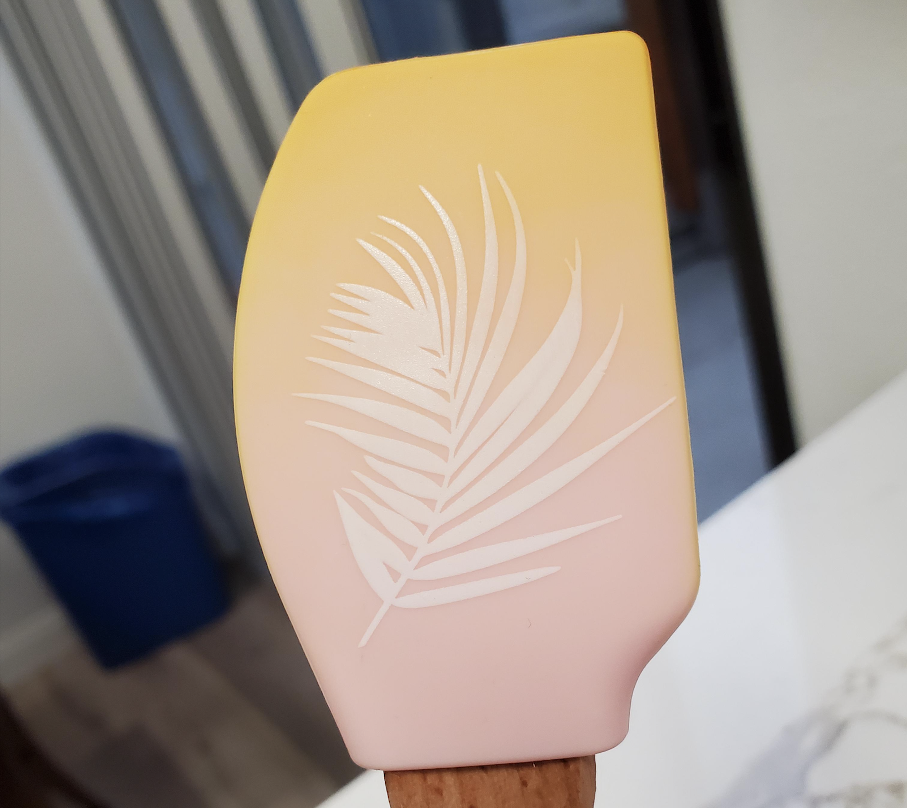 Silicone spatula with an ombre yellow-to-pink gradient and a white palm leaf pattern.