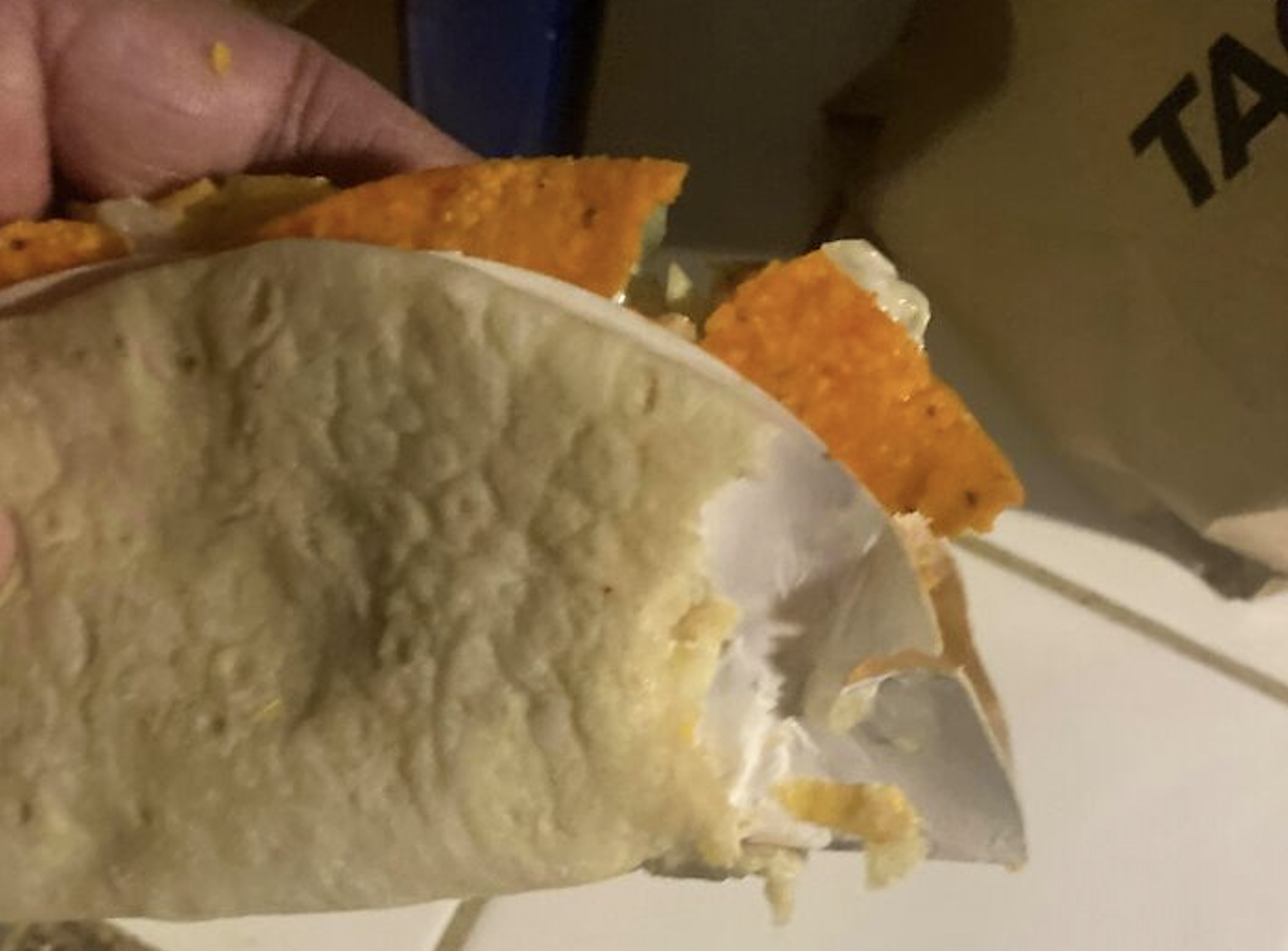 A hand holding a taco with a soft flour tortilla wrapped around a crunchy orange shell.