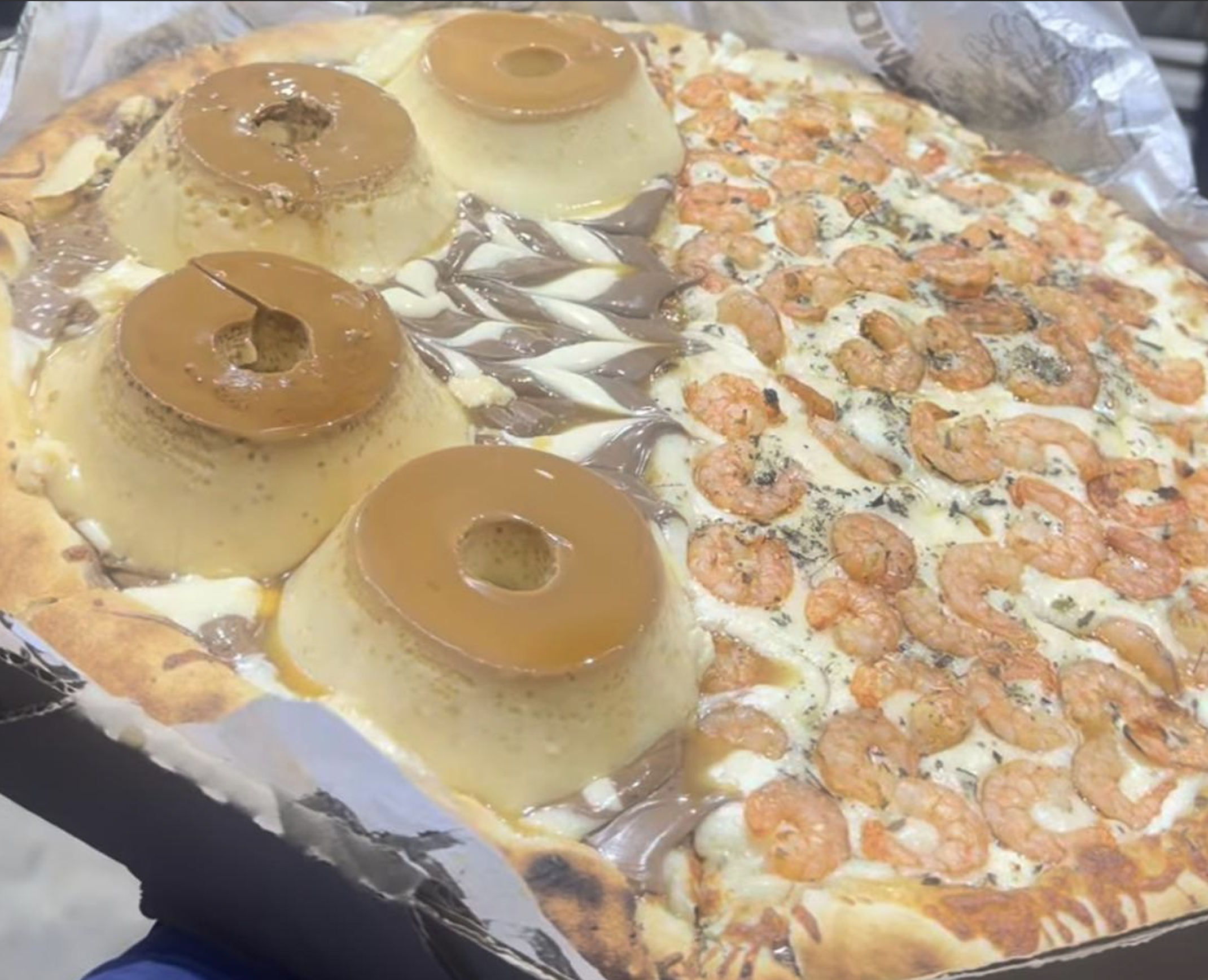 A pizza split into two halves: one topped with shrimp, and the other topped with flan and chocolate hazelnut spread.