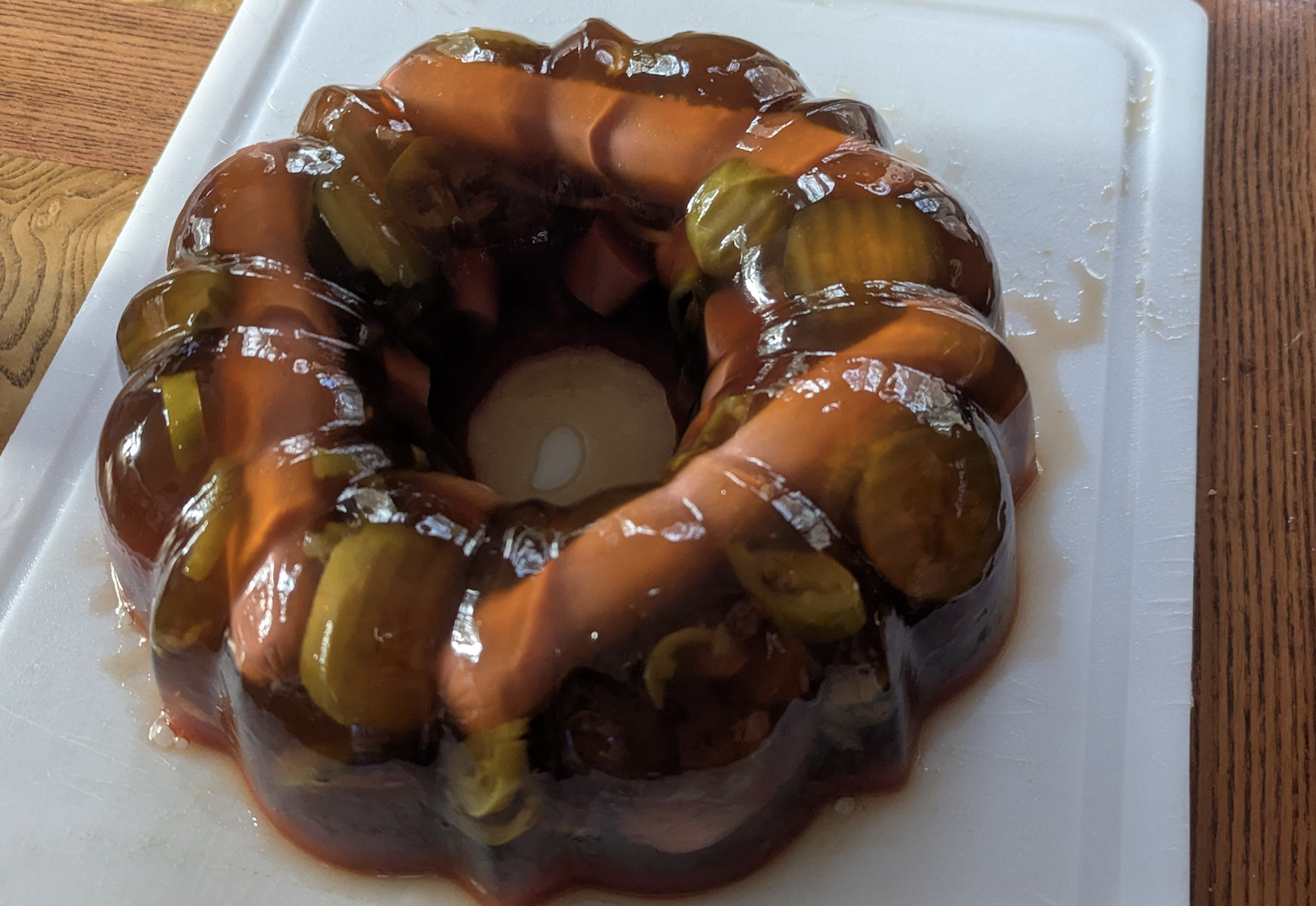 A ring-shaped gelatin mold containing sliced hot dogs and pickles.