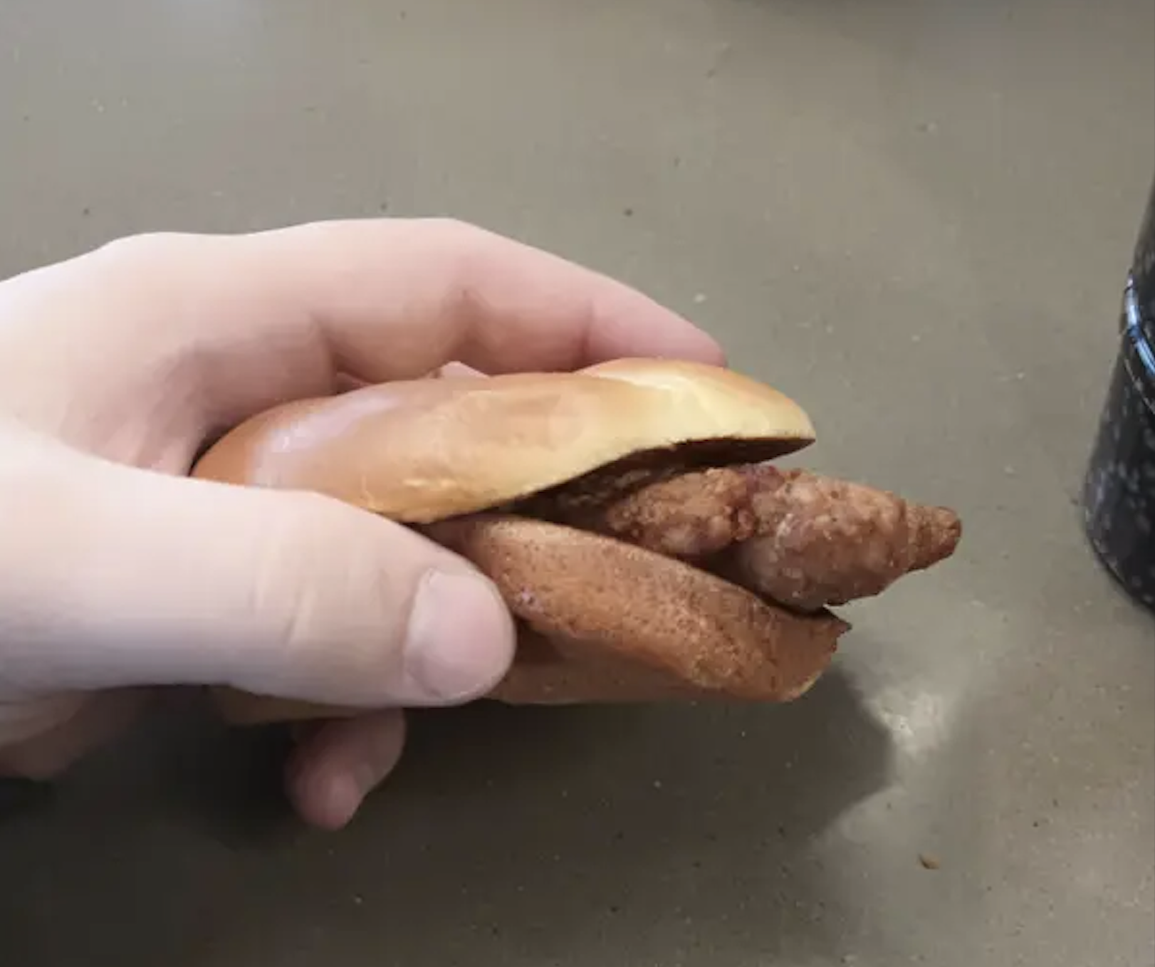 A hand holding a small, breaded chicken slider on a bun.