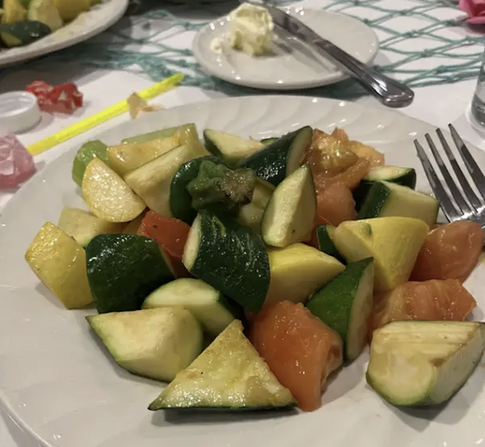 A plate of chopped sautéed zucchini, yellow squash, and tomatoes with a fork.