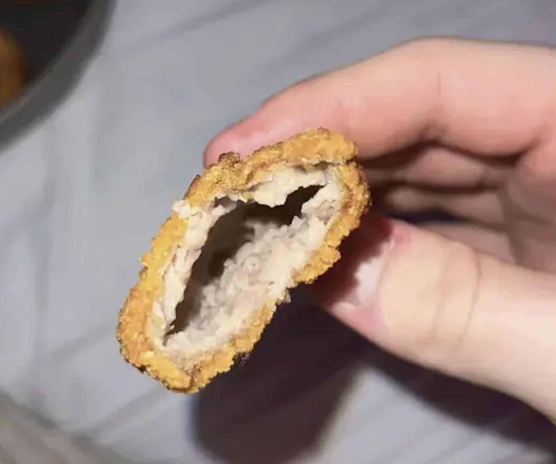 A hand holding a breaded chicken nugget that is hollow inside.