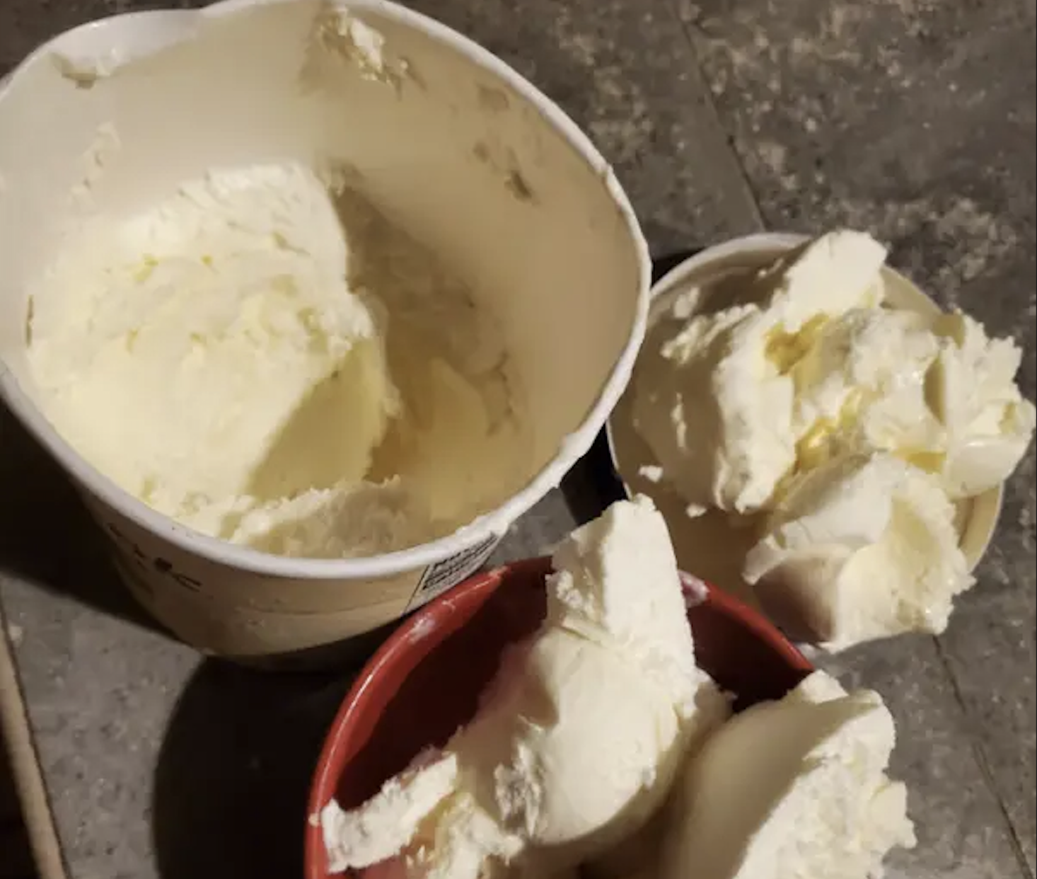 An open carton of vanilla ice cream next to a small bowl containing several scoops.