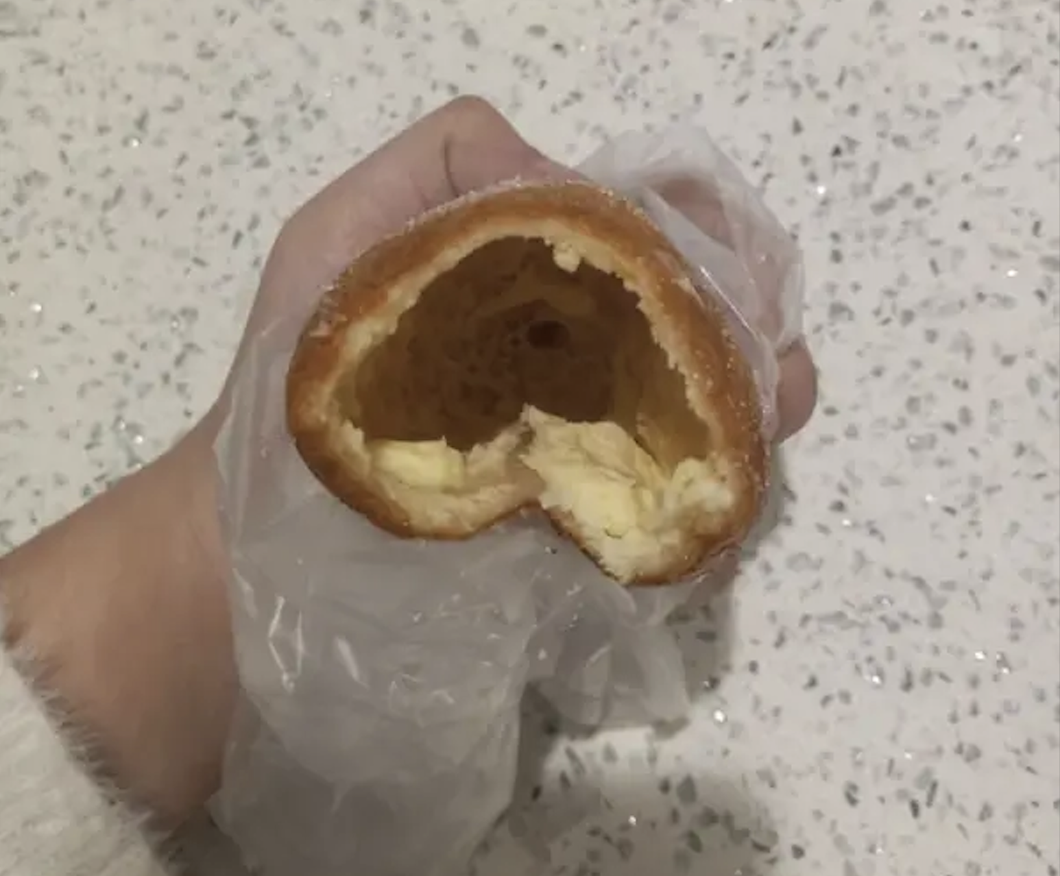 A hand in a plastic glove holds a partially eaten, hollow fried dough pastry.